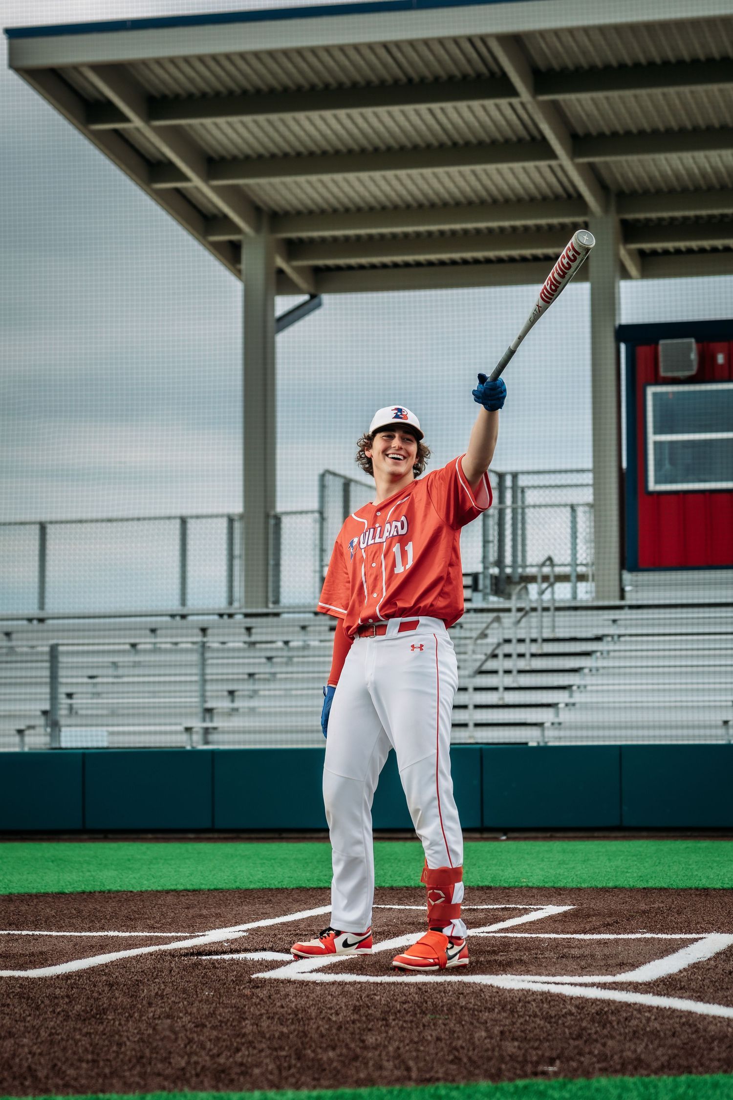 Baseball player in orange uniform holding bat up at home plate in stadium.
