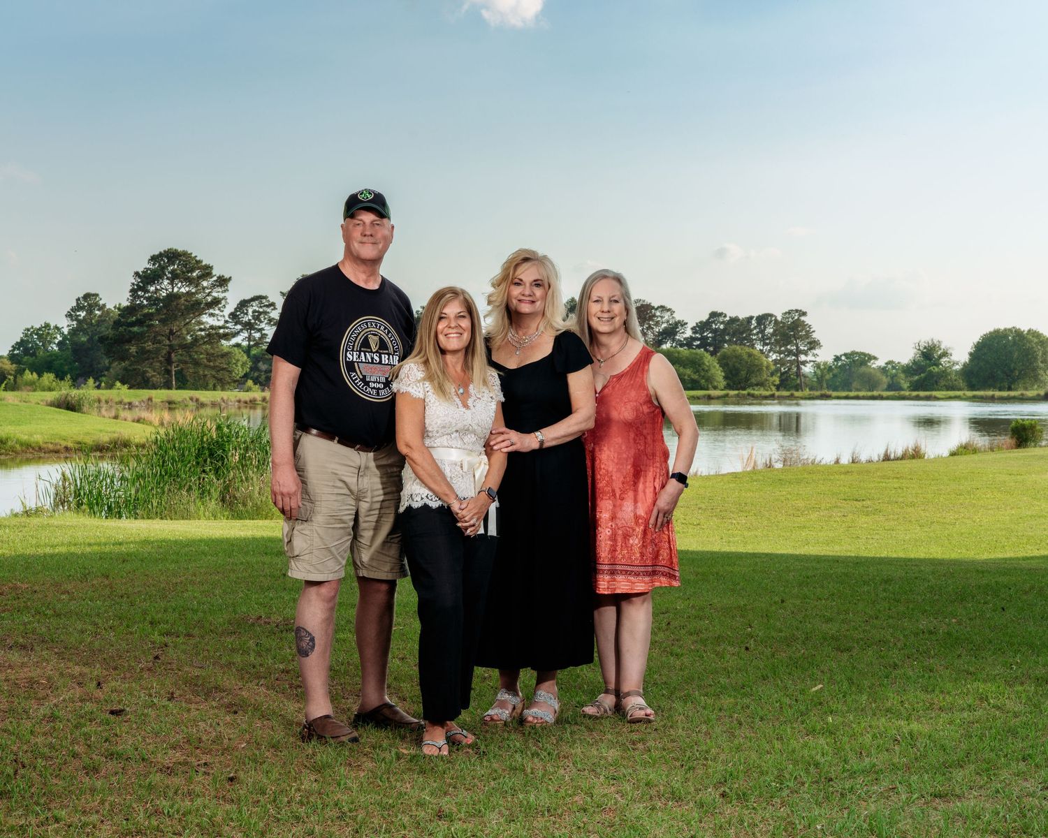 Group of four adults standing together on green grass near a peaceful pond at dusk.