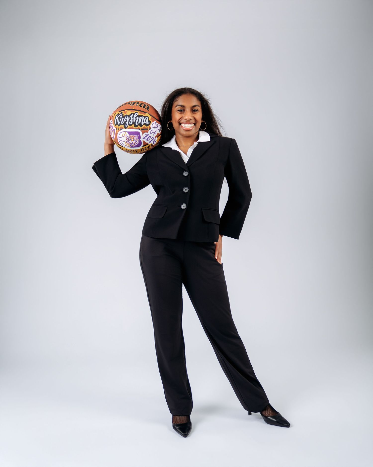 A smiling woman in a black business suit holds a decorative basketball while posing in a bright studio.