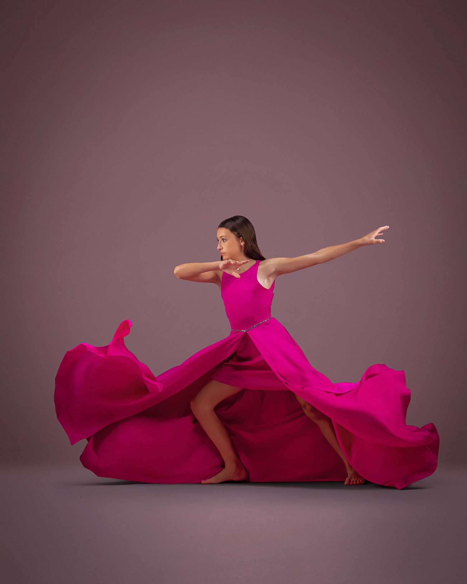 A dancer in a flowing magenta gown strikes a dramatic pose, arms extended, fabric swirling around her on a mauve background.