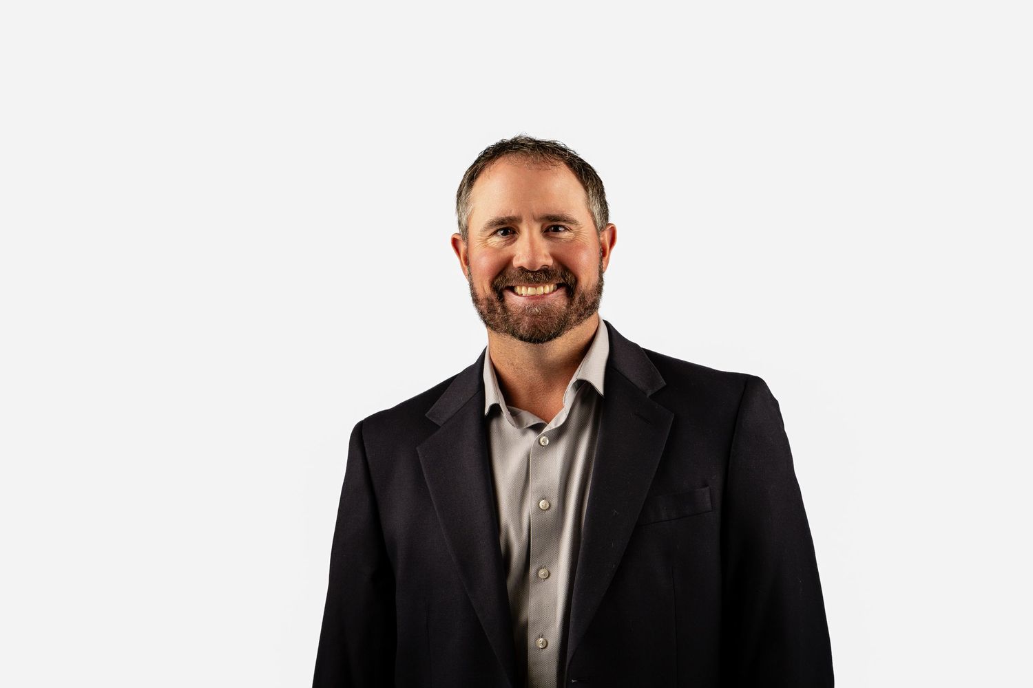 Professional businessman in black blazer smiling confidently against white background.