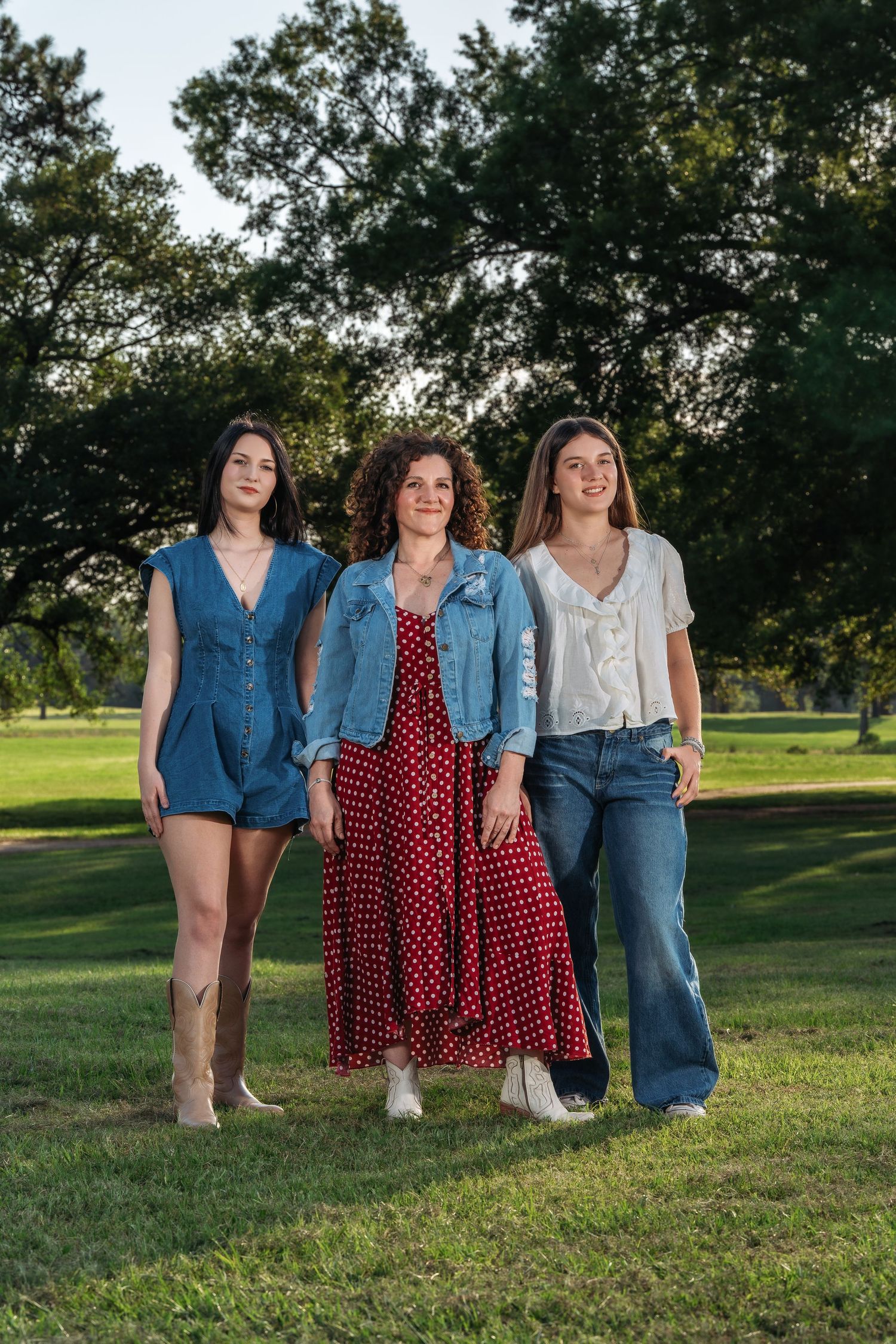 Three women smiling and walking together in a sunny green park setting.