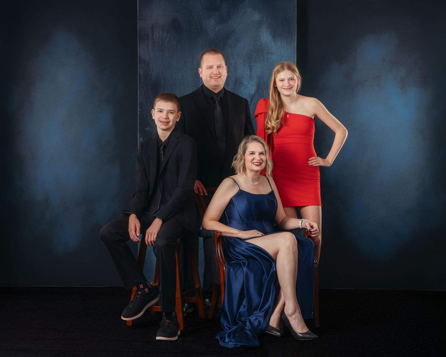 Family of four dressed formally posing together against a dark blue textured studio background.