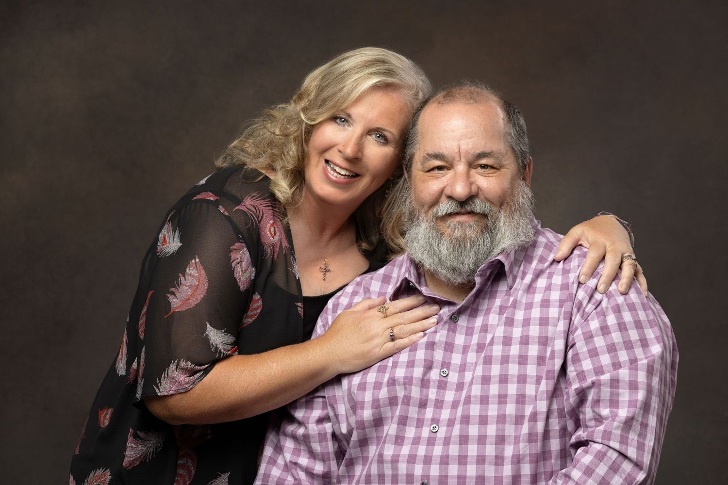 Smiling couple posing together, woman with blonde hair embracing bearded man in pink shirt.