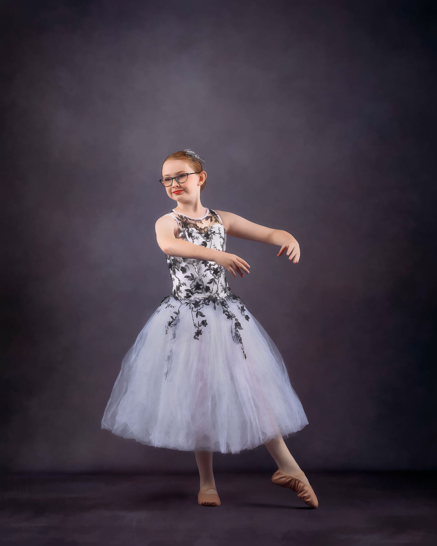 Young dancer in white and black floral tutu performs on studio backdrop.