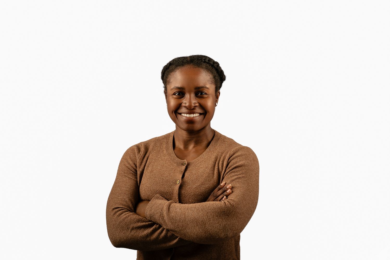 Smiling woman with braids in brown cardigan posing with arms crossed on white background.