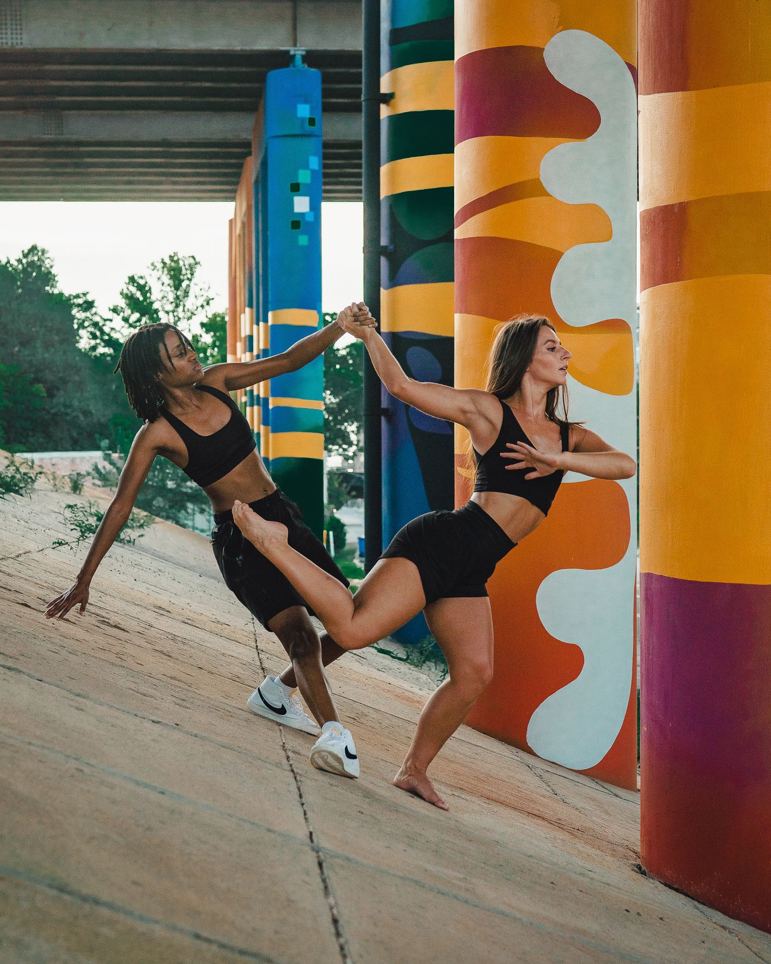 Two women in black athletic wear dancing near colorful mural pillars.