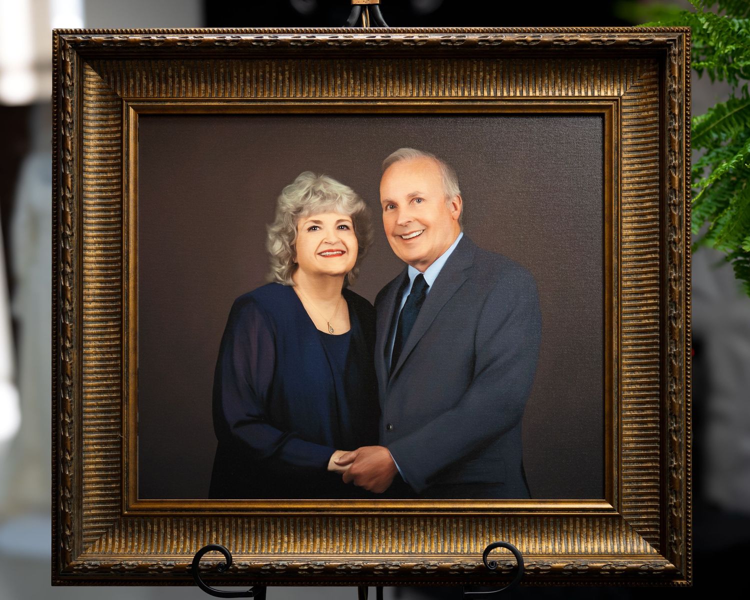 Gold ornate framed portrait of a smiling elderly couple in formal attire on a display easel.