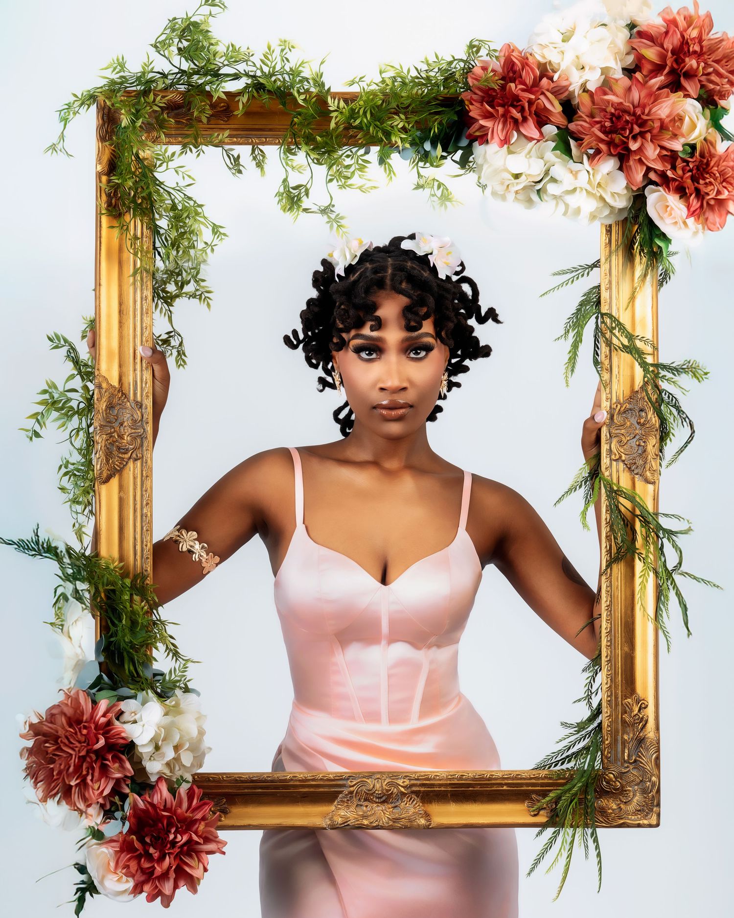 Woman in pink satin dress poses inside gold ornate frame with floral decorations.