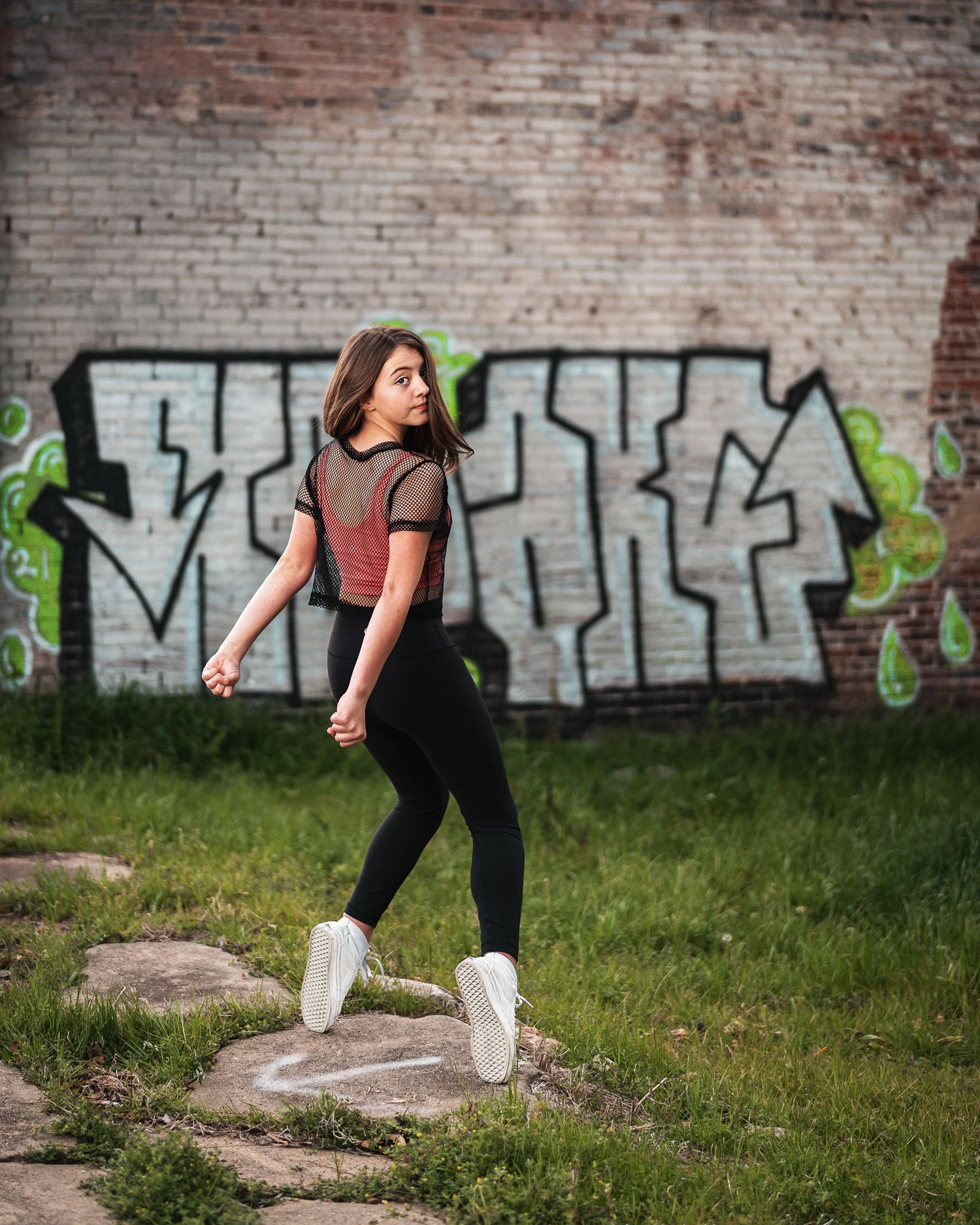 Teen girl in black leggings walking past colorful graffiti brick wall.