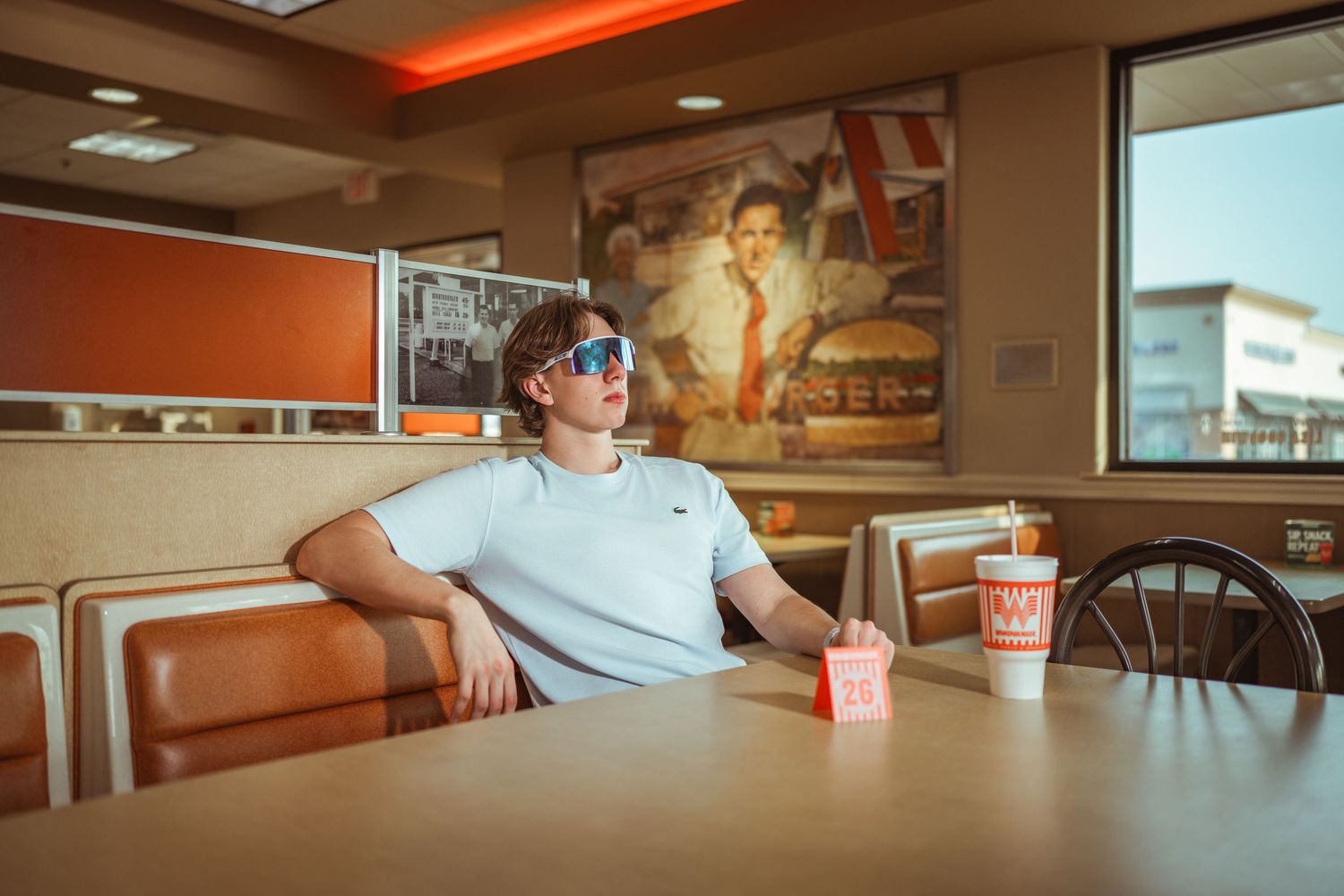 Young man in sunglasses relaxing in a Whataburger booth with food and drinks.