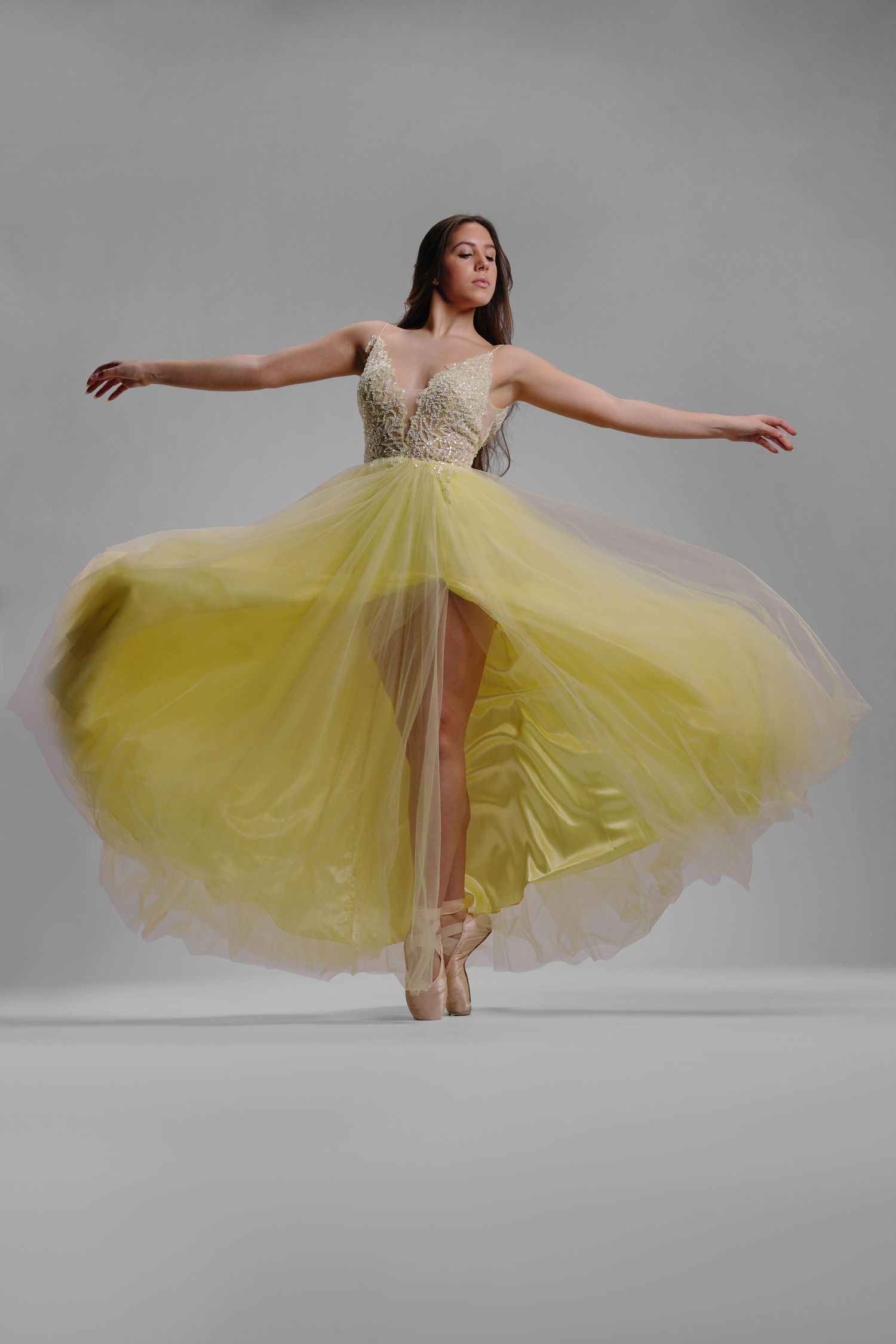 Graceful ballerina in flowing yellow tulle gown dancing on pointe shoes against gray background.