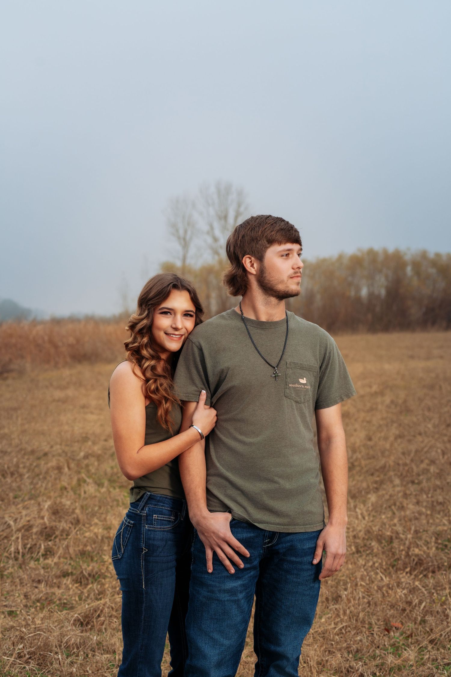 Young couple posing romantically in an open field with bare trees on a foggy day.