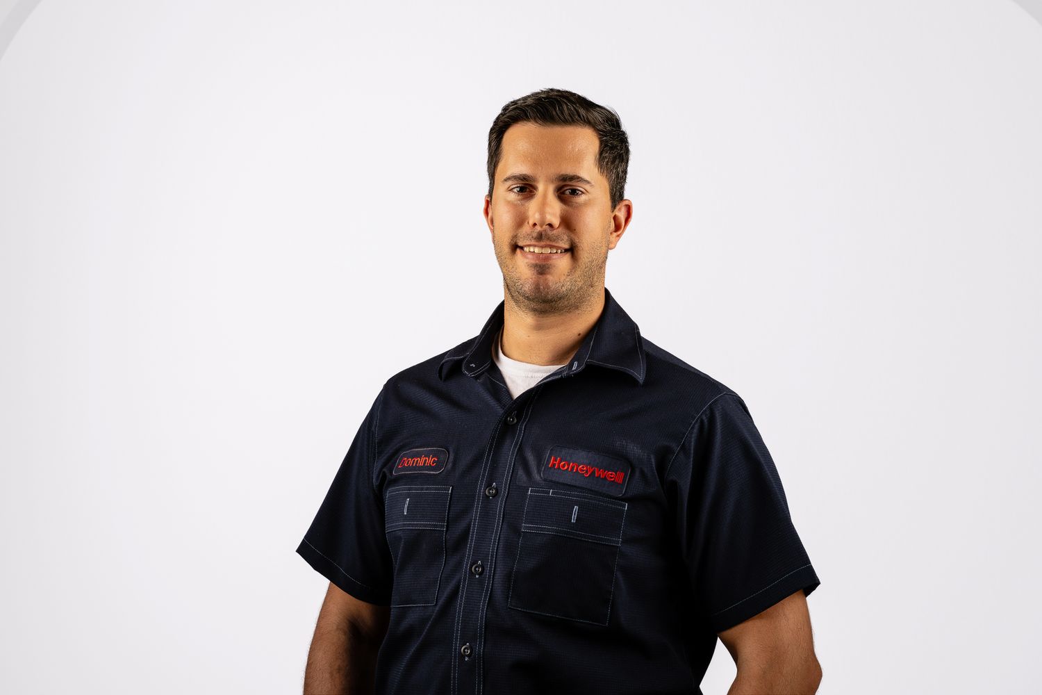 Smiling man in navy embroidered work shirt posing against white background.