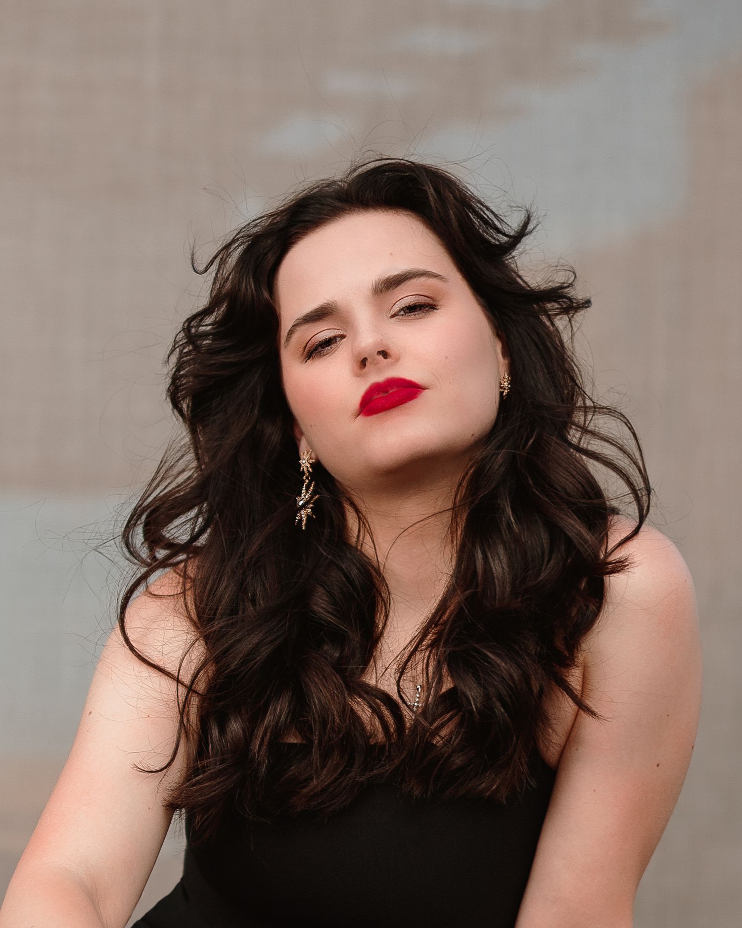 Elegant woman with dark wavy hair and bold red lips poses in a black strapless top outdoors.