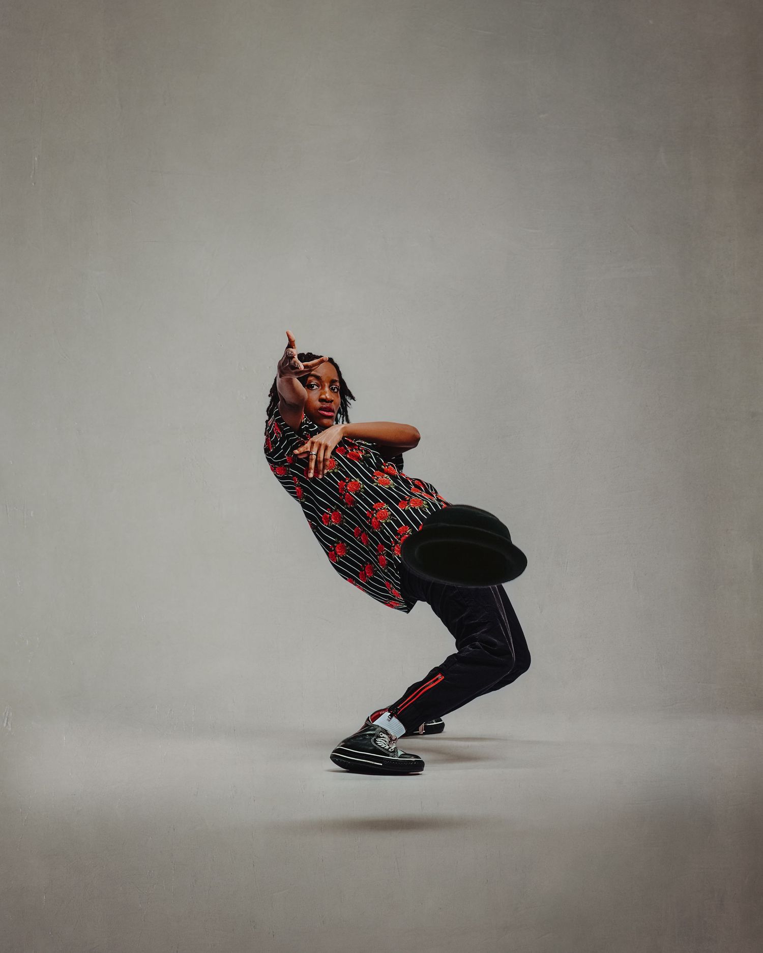 Hip-hop dancer in a red patterned outfit performing a dynamic low crouch move in a studio.