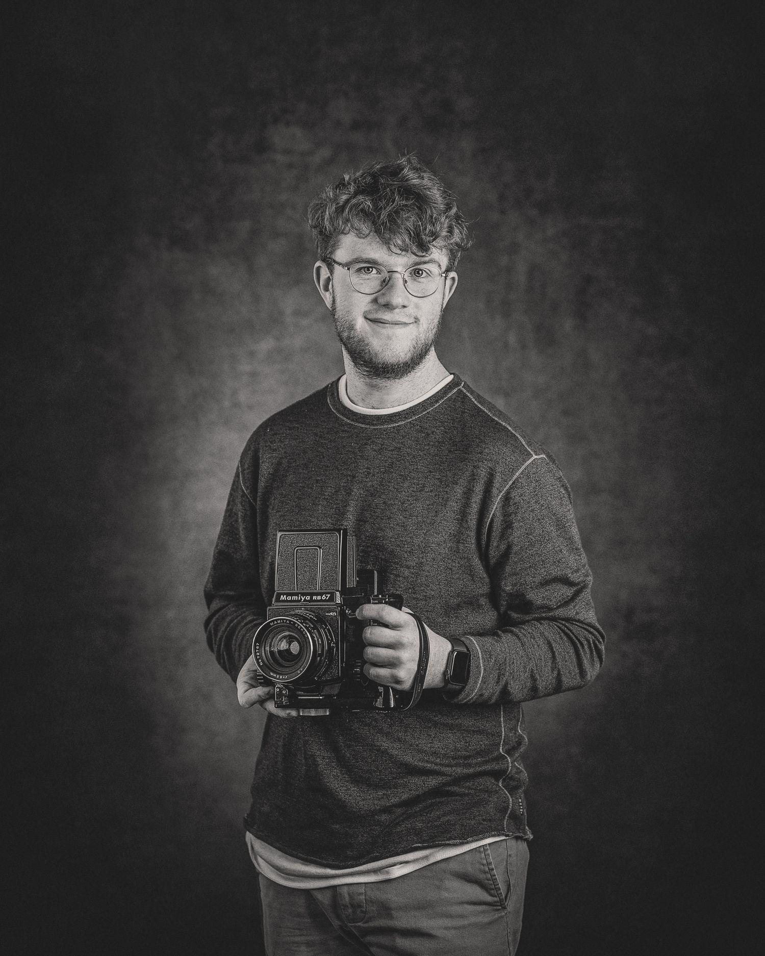 Young man holding vintage medium format camera in black and white portrait photo.