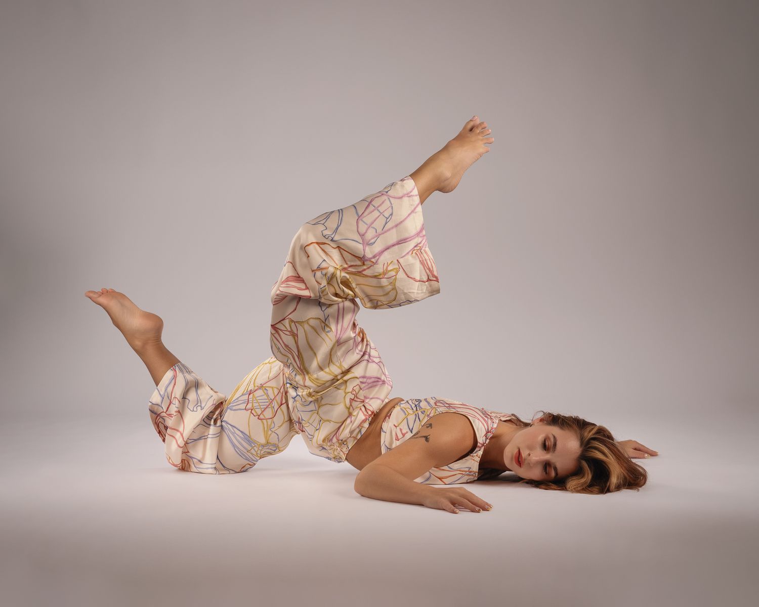 Female contemporary dancer lying on the floor in a floral outfit with leg raised in studio.