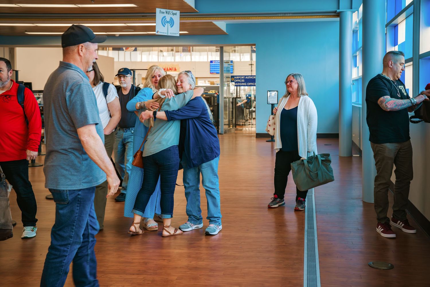 Group of people greeting each other with hugs in a busy airport terminal.
