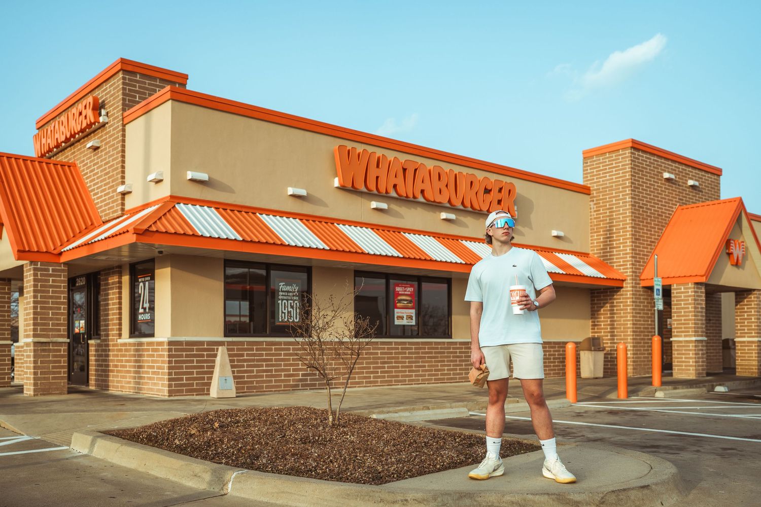 Young man holding a drink standing outside a Whataburger restaurant on a sunny day.