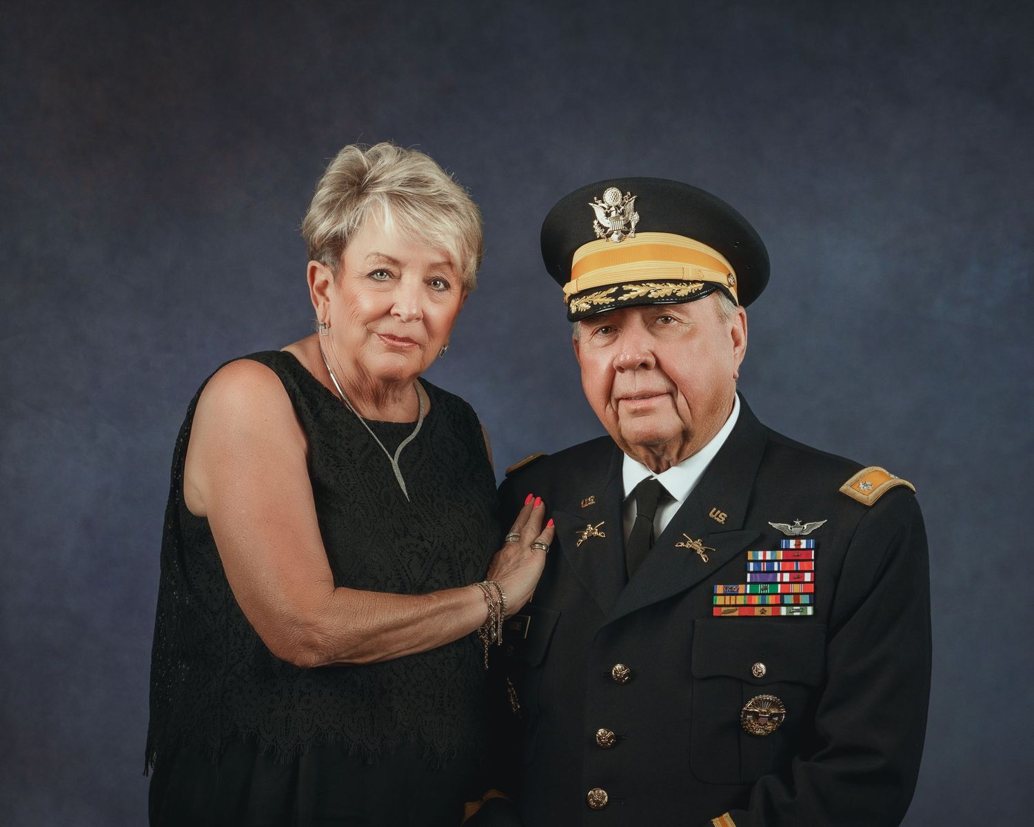 An elderly couple poses formally, the man wearing a decorated military dress uniform.
