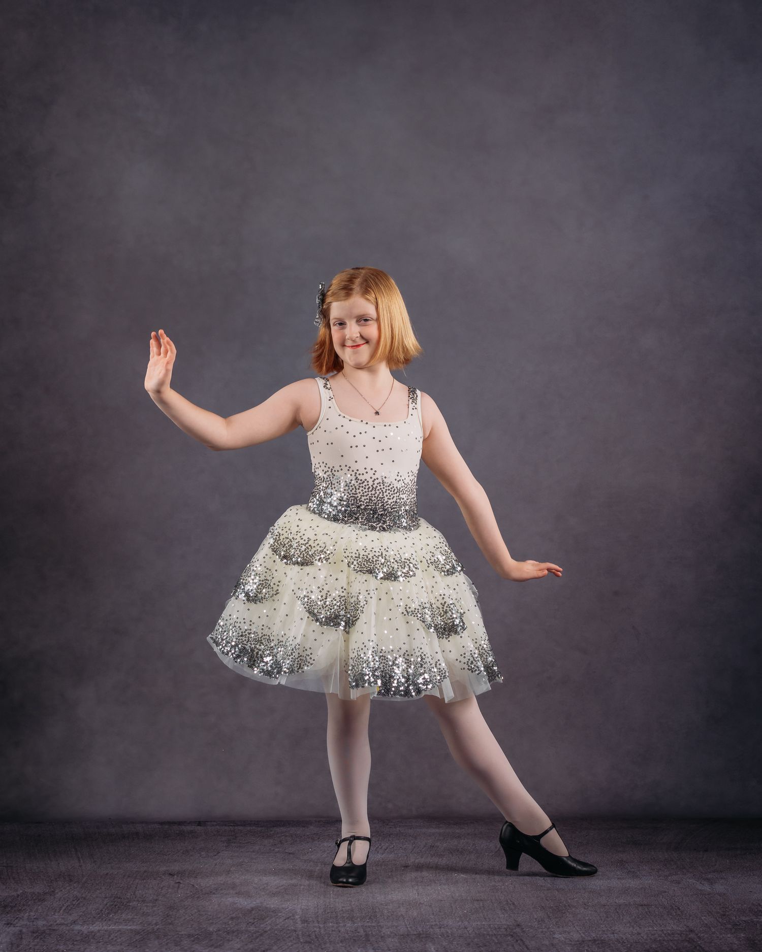 Young girl in a sparkling white tiered dance costume posing with a smile in a studio.
