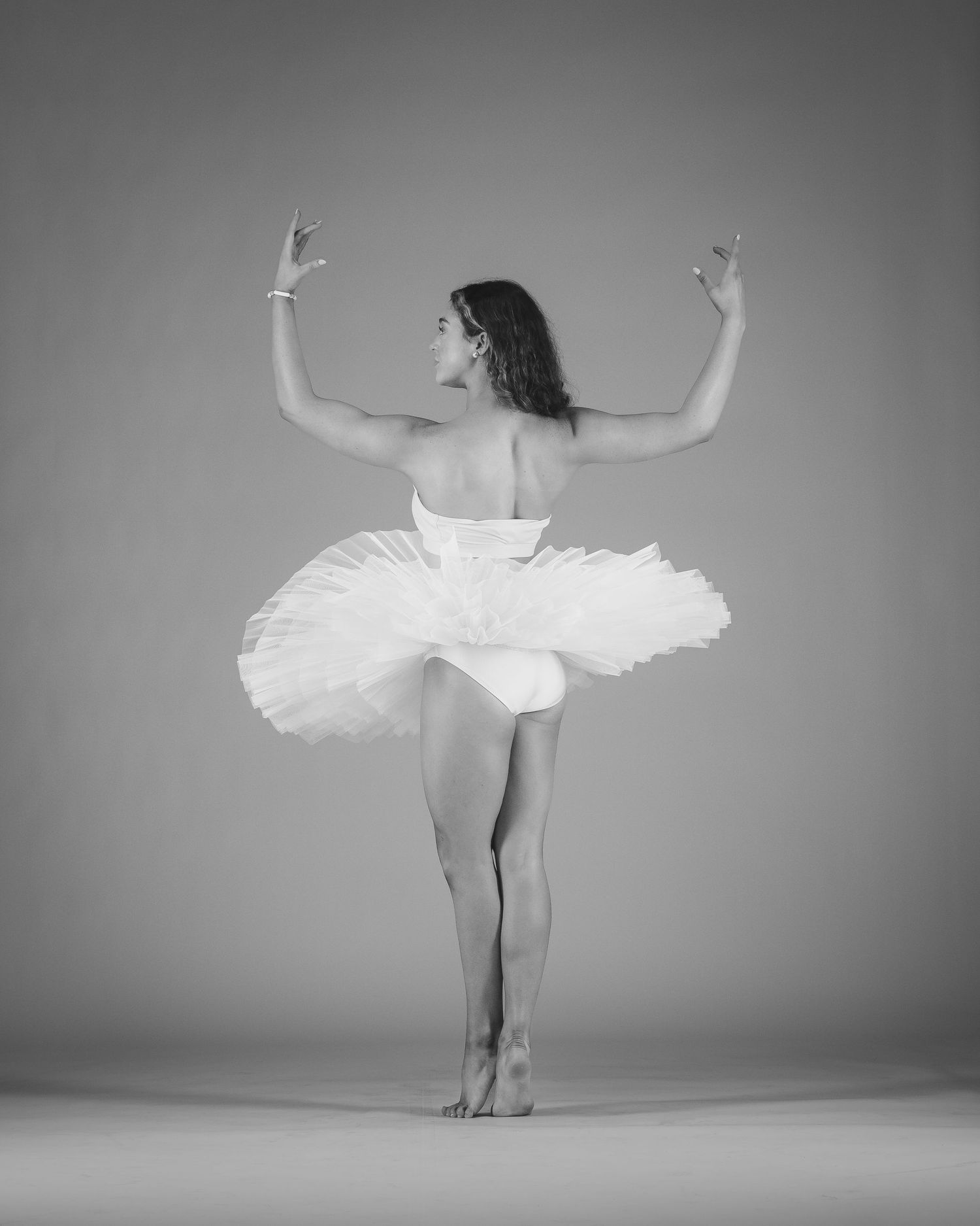 Black and white photo of a ballerina in a white tutu performing an elegant pose on one leg with arms raised.