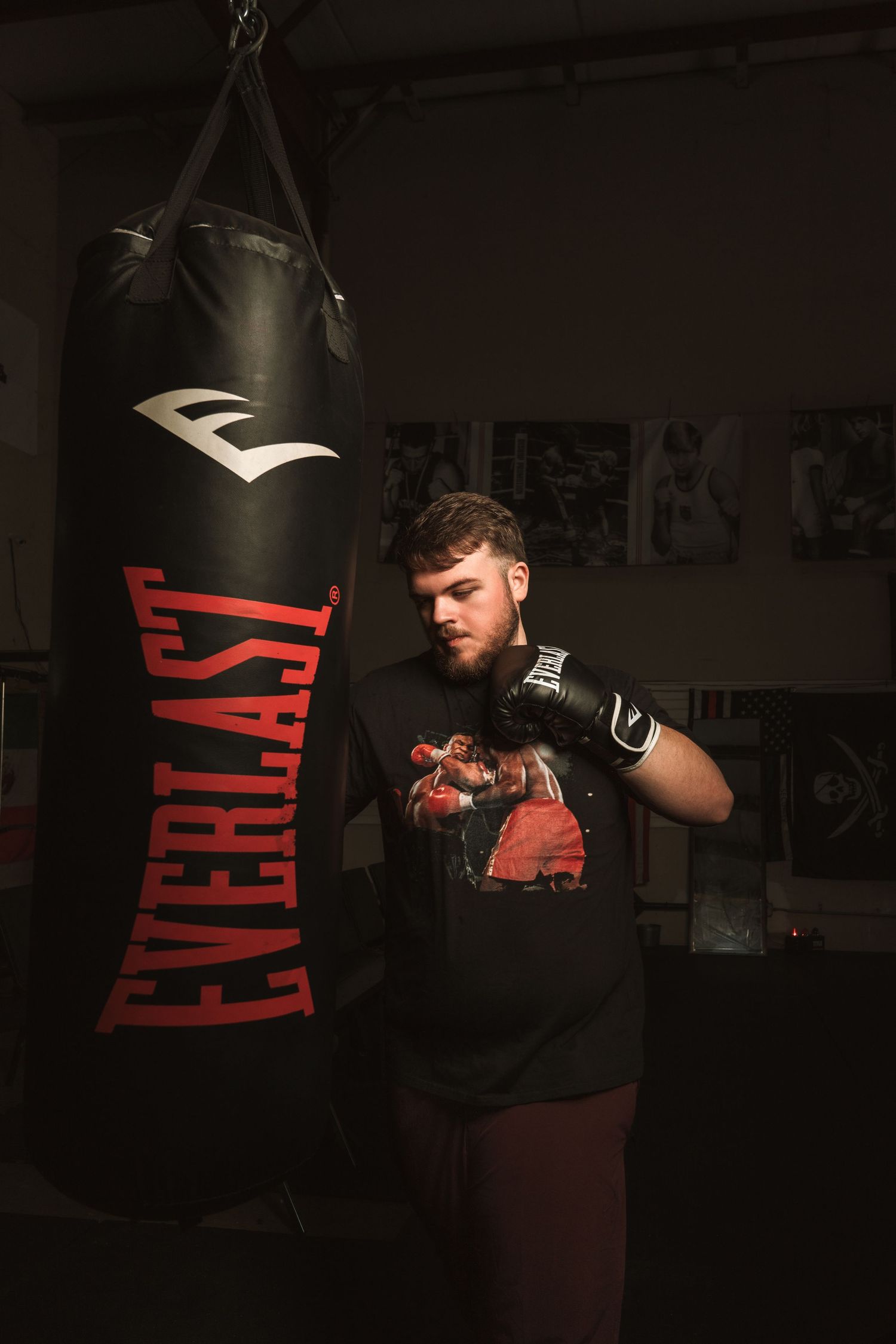Young male boxer training with an Everlast heavy punching bag in a dark gym.
