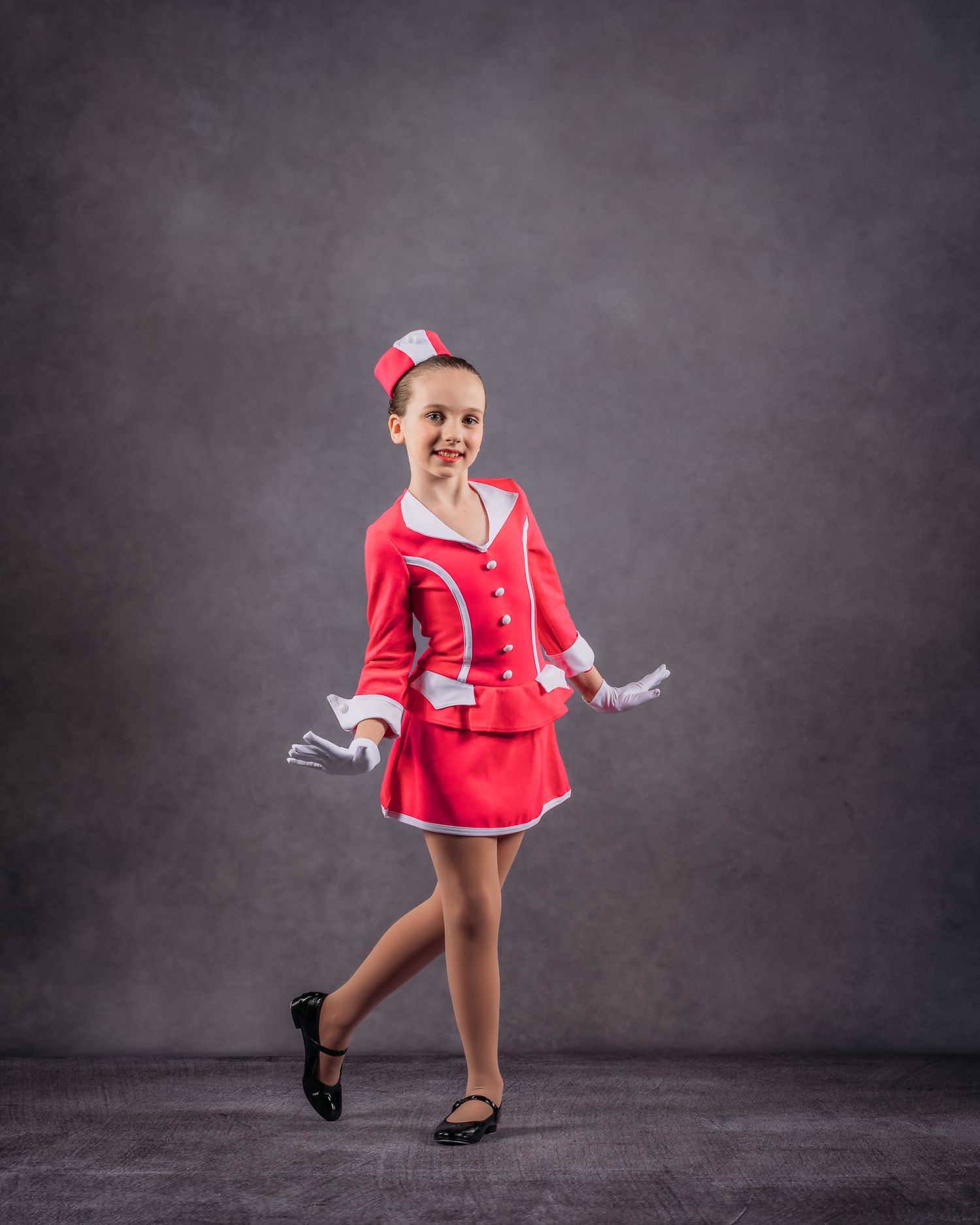 Young girl in a red majorette costume posing confidently in a dance studio portrait.