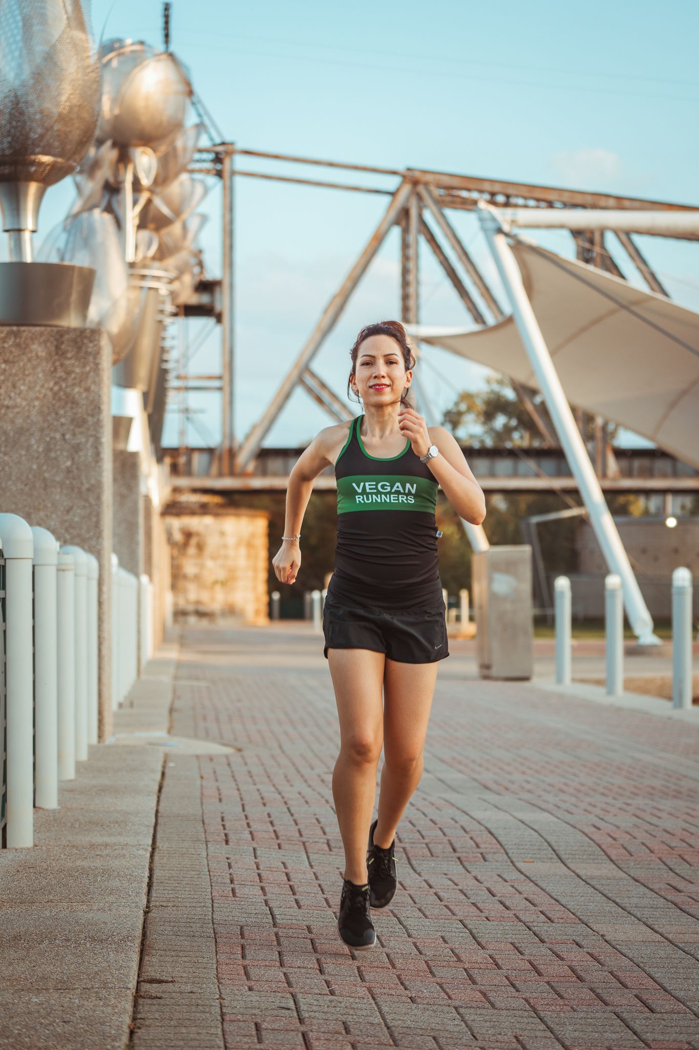 Female runner in Vegan Runners tank top jogging along urban waterfront pathway outdoors.