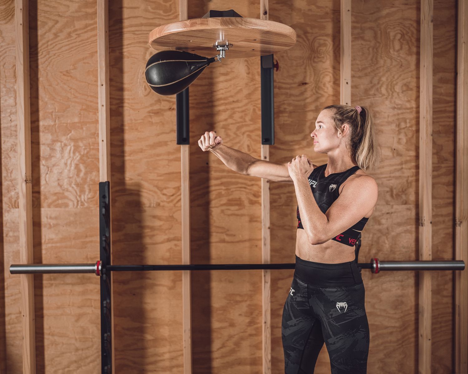 Athletic woman training with a speed bag on a wall-mounted platform in a rustic gym.