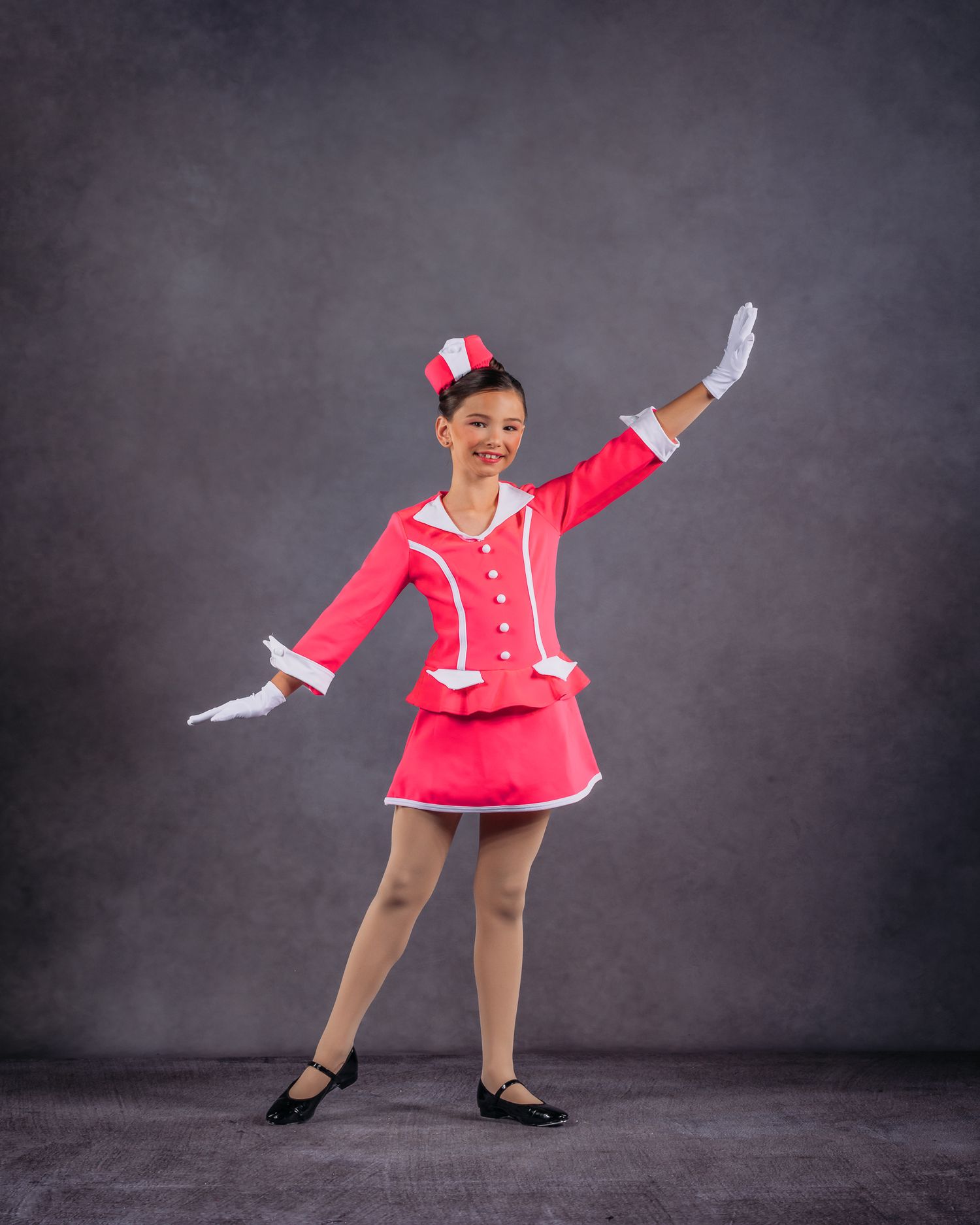 Young dancer in pink majorette costume with hat and white gloves performs jazz dance pose.