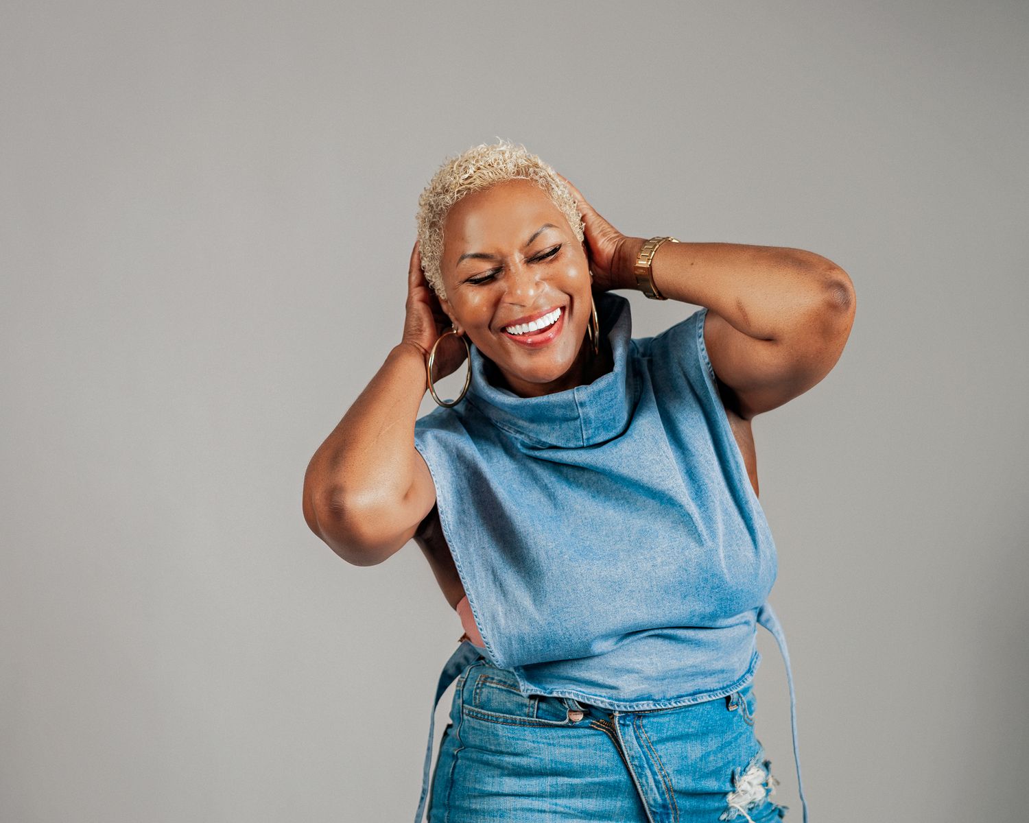 Joyful Black woman with blonde hair laughing on gray studio background.
