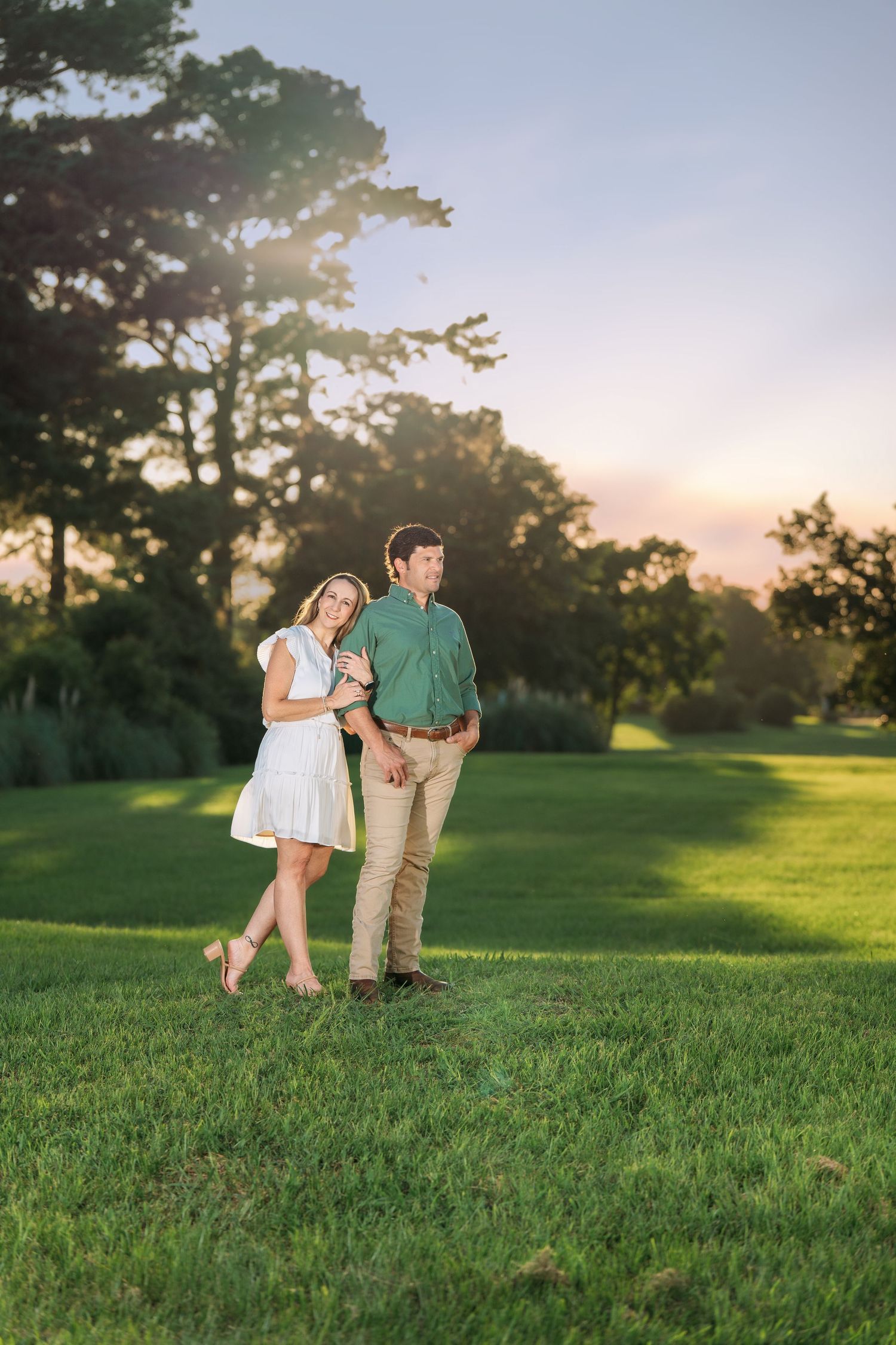 A couple walks hand-in-hand on a green lawn during a beautiful golden hour sunset outdoors.