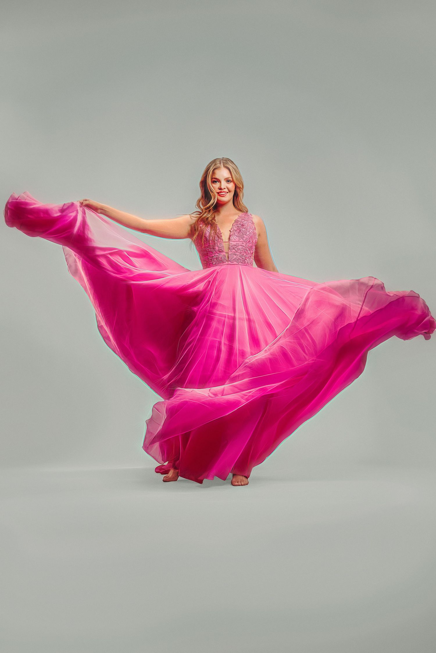Woman twirling in a flowing pink chiffon gown with beaded bodice against gray background.