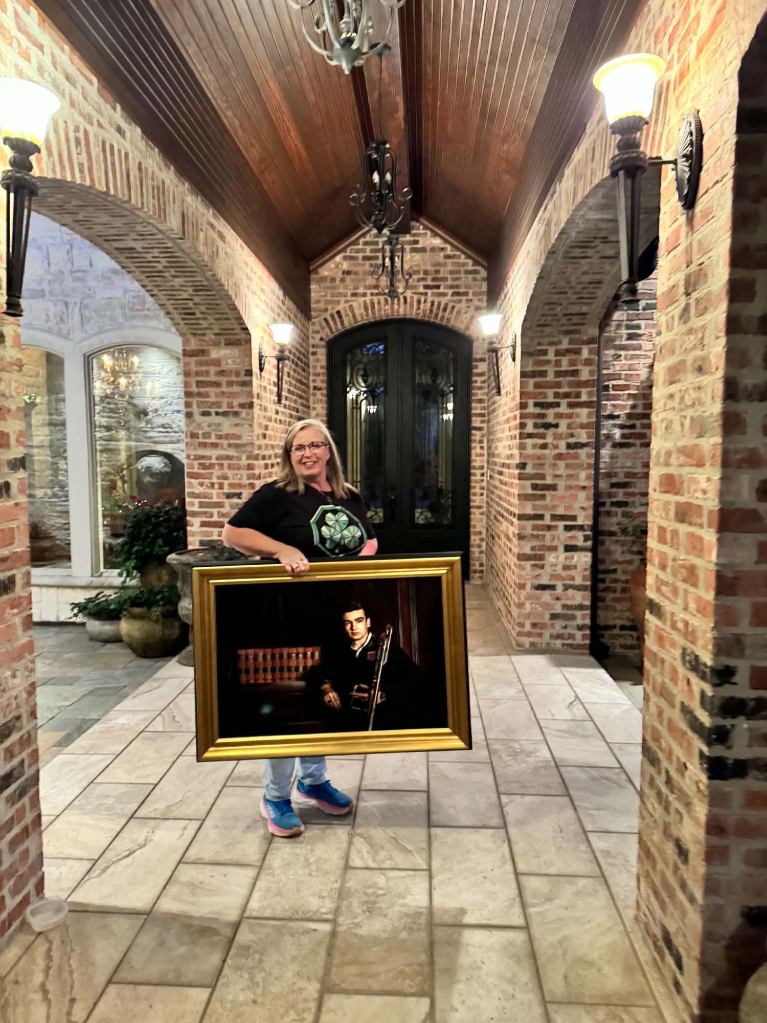 Woman holds a large gold-framed portrait of a man with guitar in an elegant brick archway.