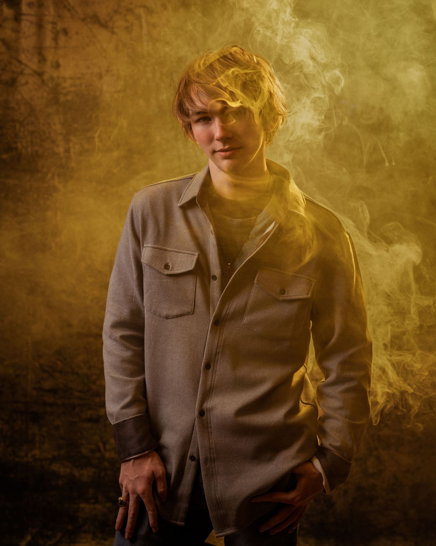 Young man in grey shirt surrounded by golden smoke in dramatic portrait.