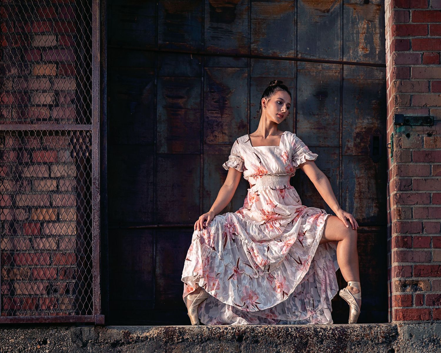 Dancer in floral dress poses gracefully on windowsill against rustic brick wall.