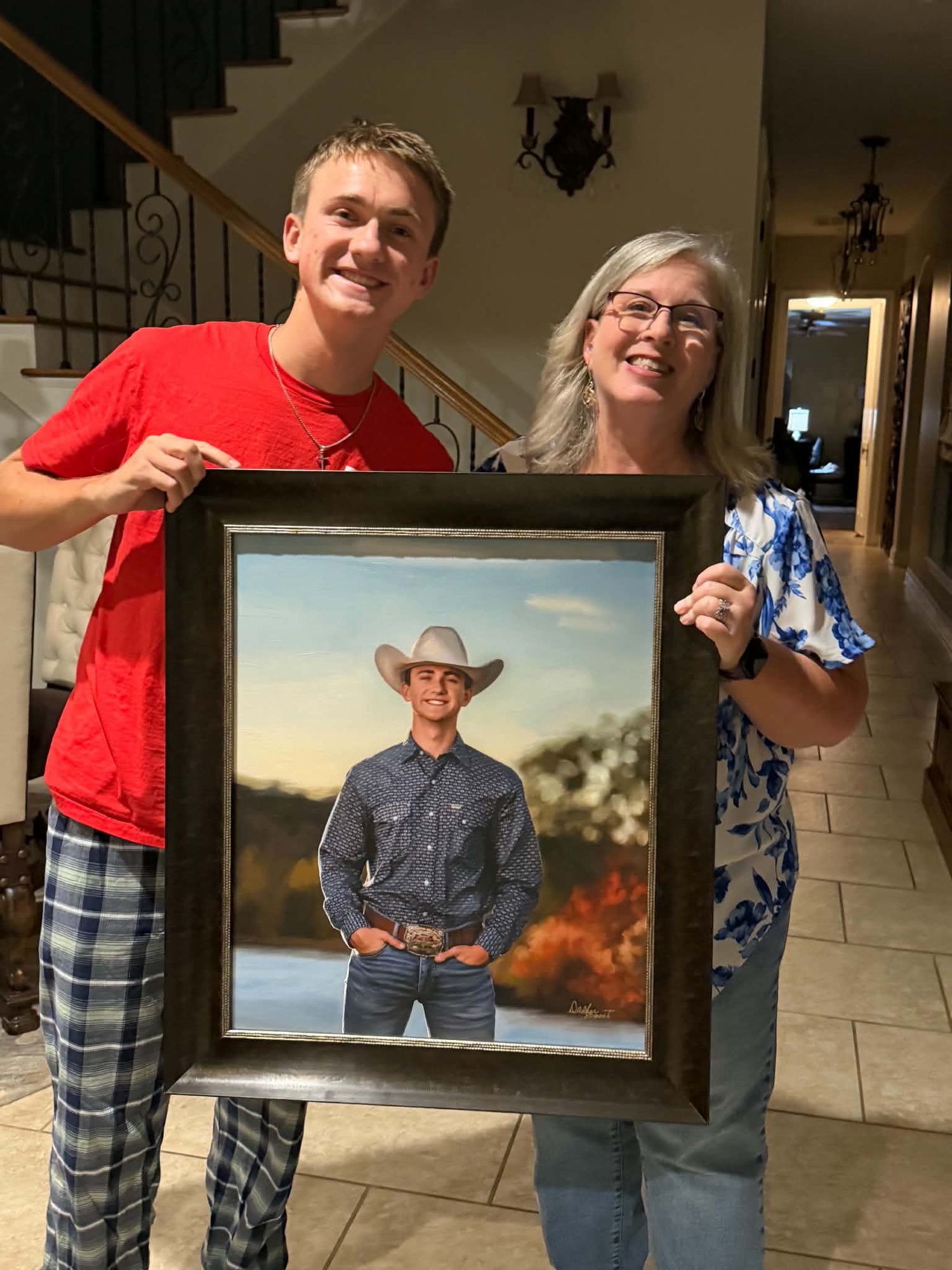 Mother and son proudly holding a large framed portrait of a young man in a cowboy hat.