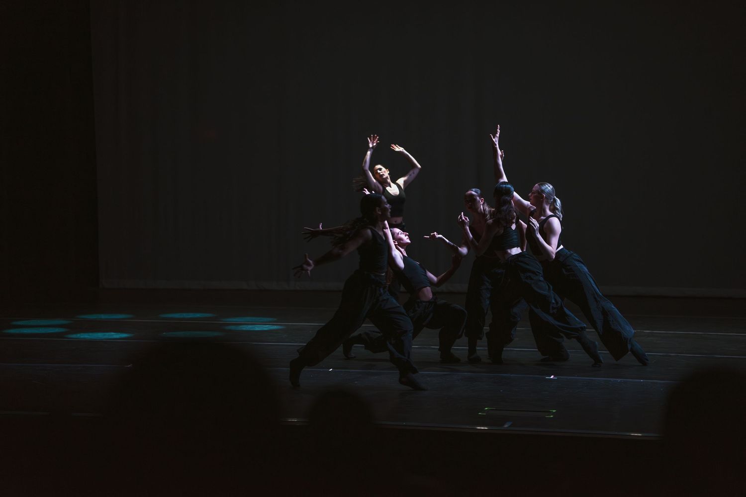 Dancers in black costumes perform a dramatic contemporary dance routine on a dimly lit stage.