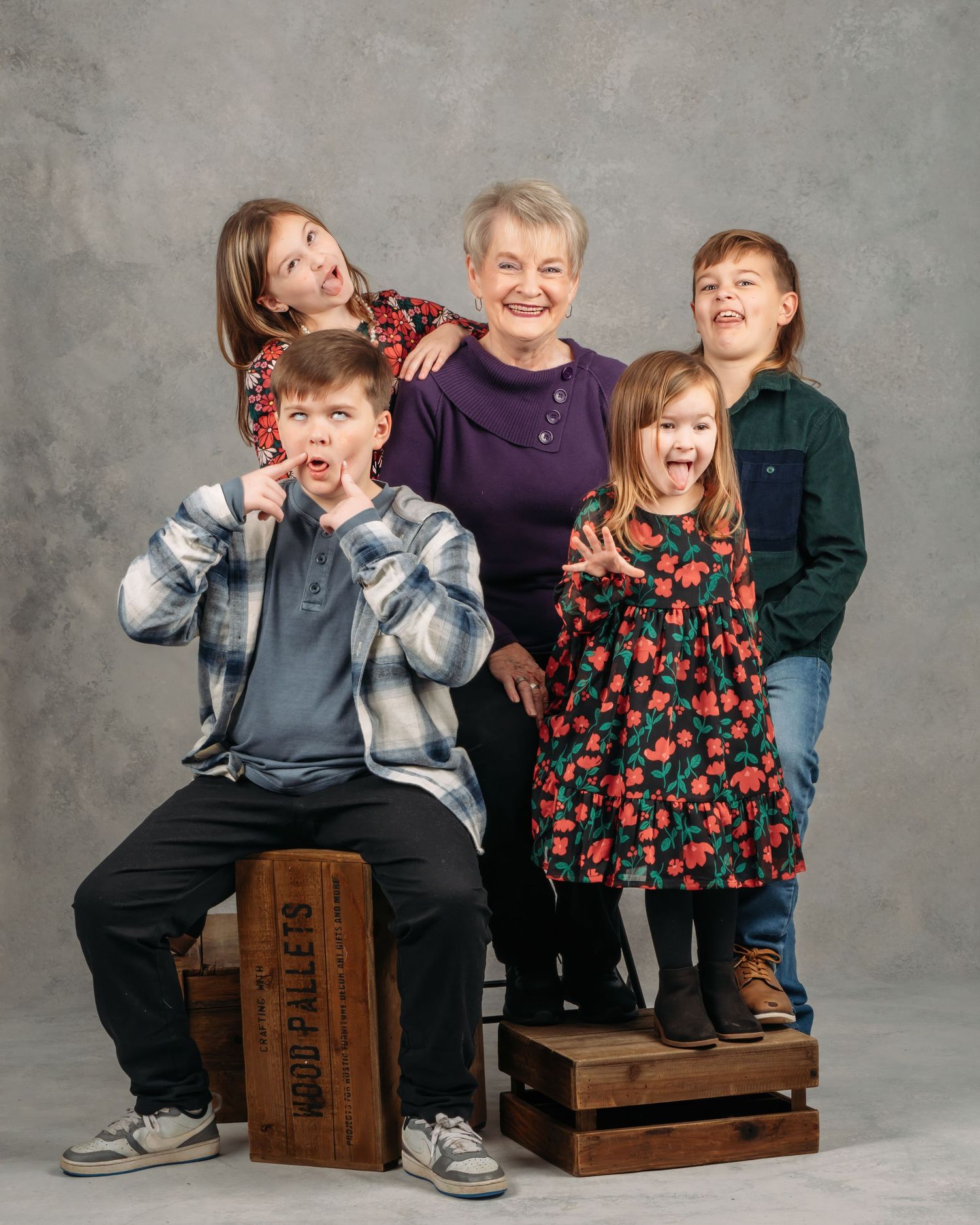 A grandmother and four grandchildren make silly faces in a fun studio portrait.