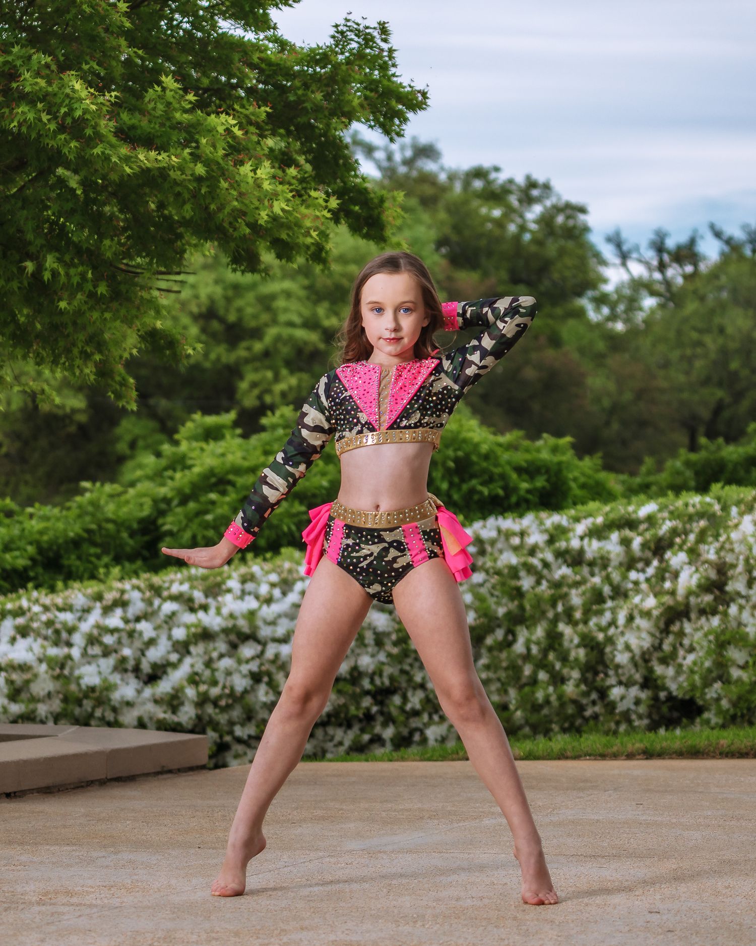 Young dancer in pink and black costume performing dance pose on outdoor stage.