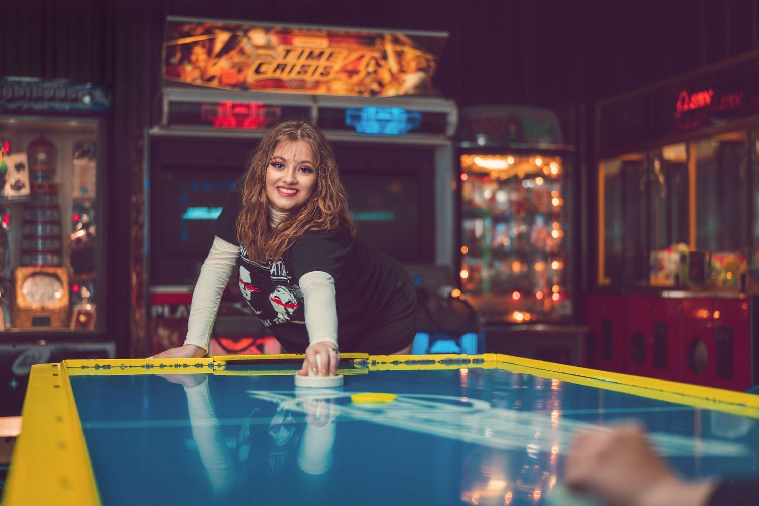 Smiling young woman plays air hockey in a colorful retro arcade game room.