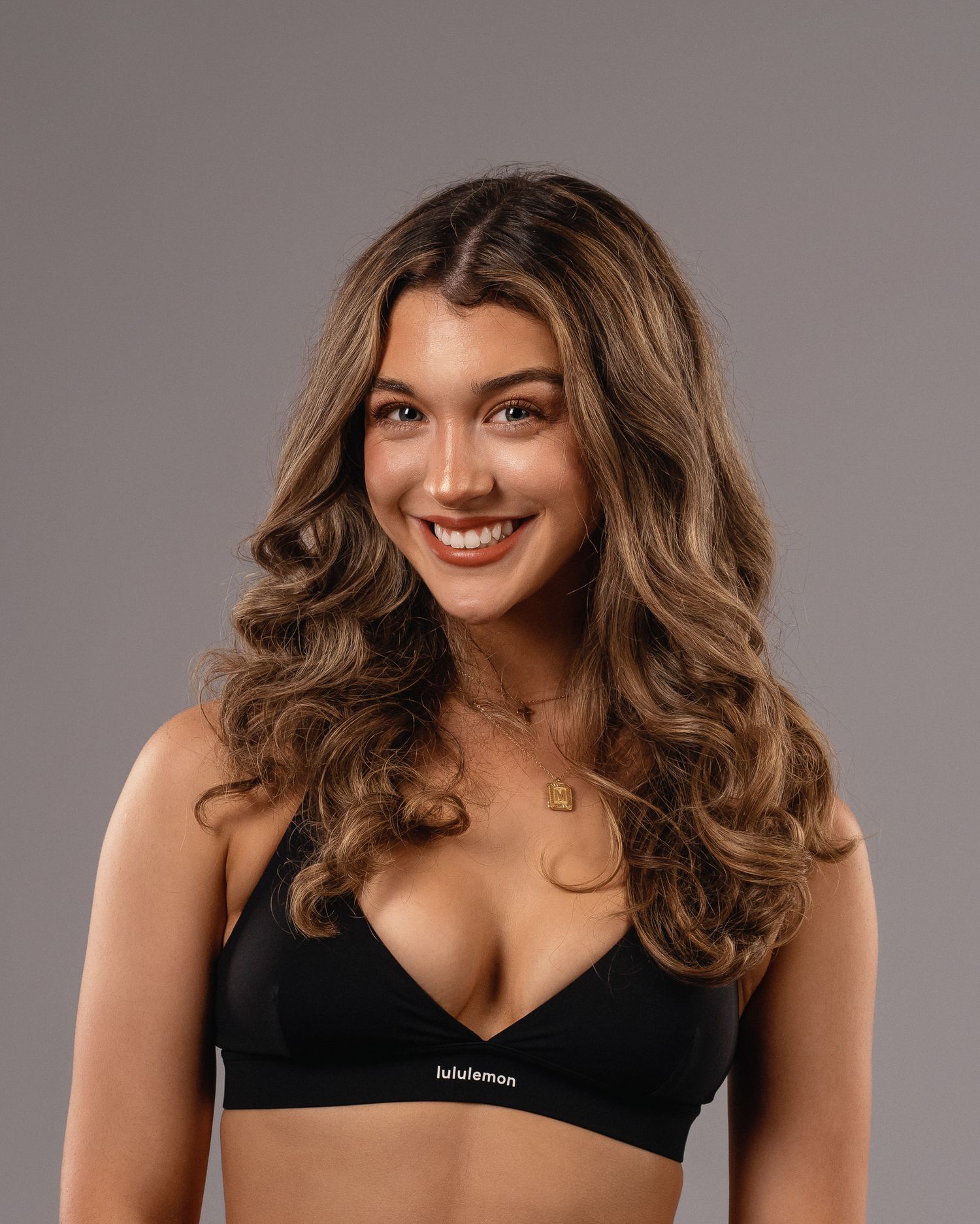 Young woman with long wavy hair smiling wearing a black Lululemon sports bra.