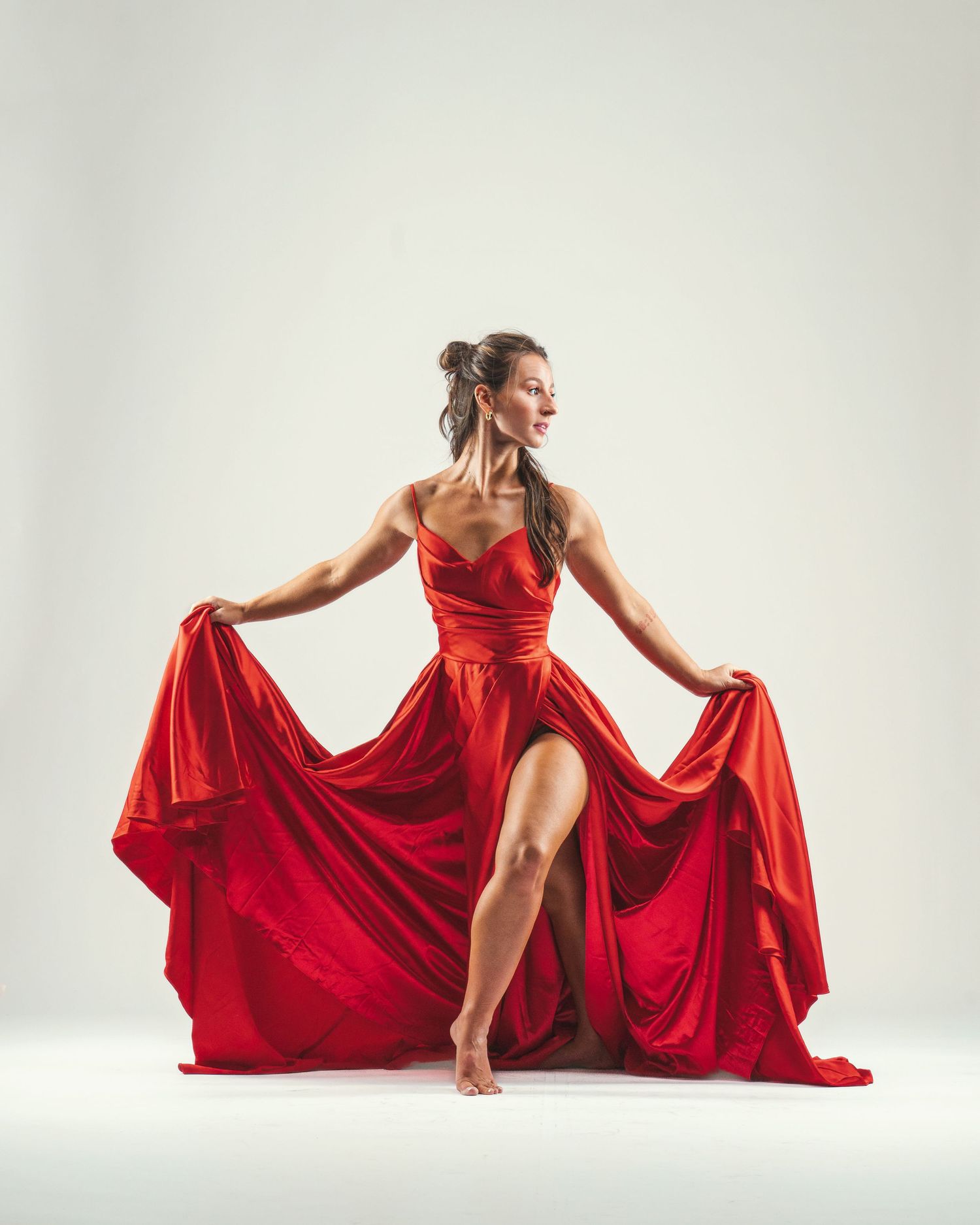 Woman in flowing red gown gracefully dancing, holding dress sides wide in elegant studio pose.