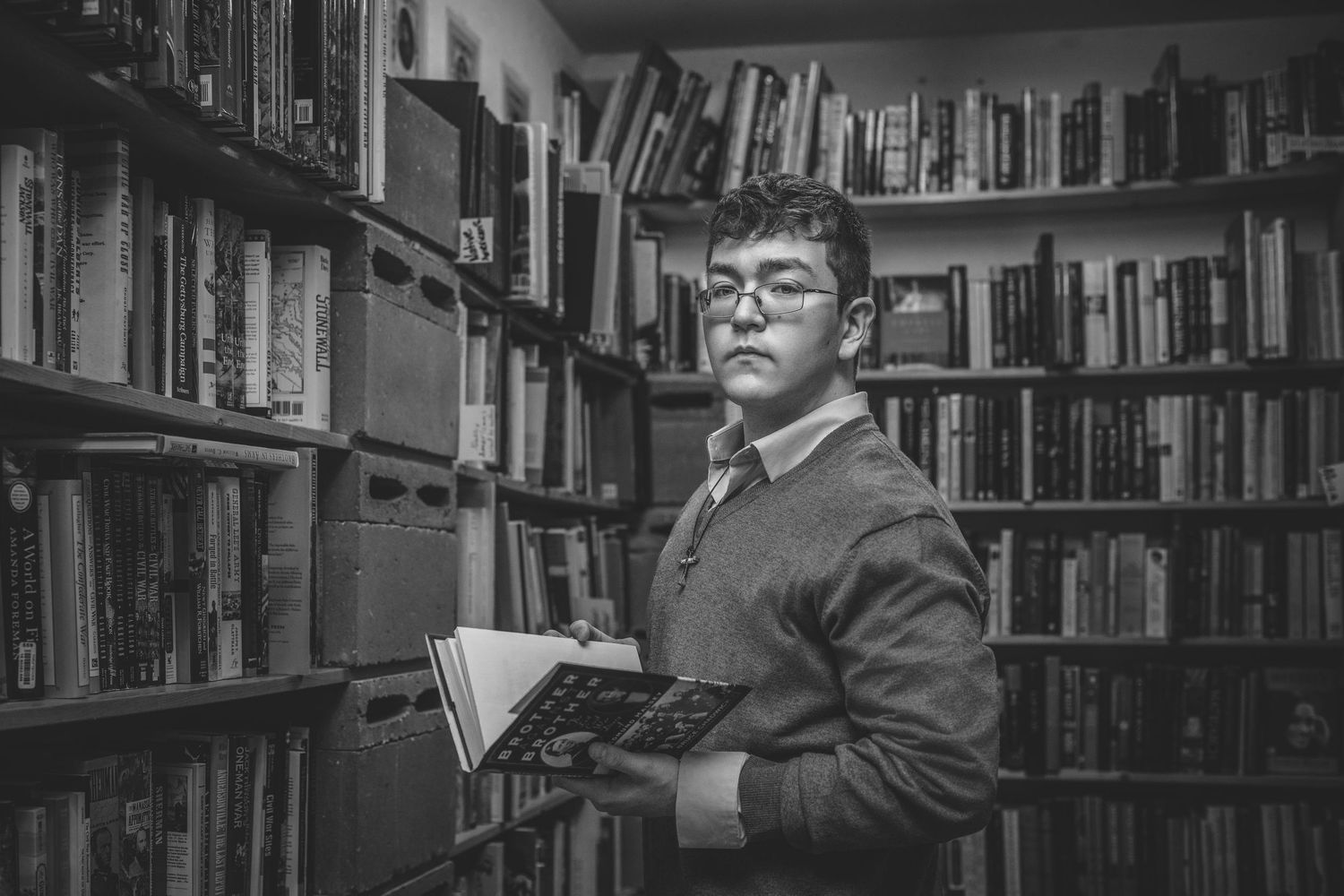 Man with glasses holding a book in a black and white bookstore library setting.