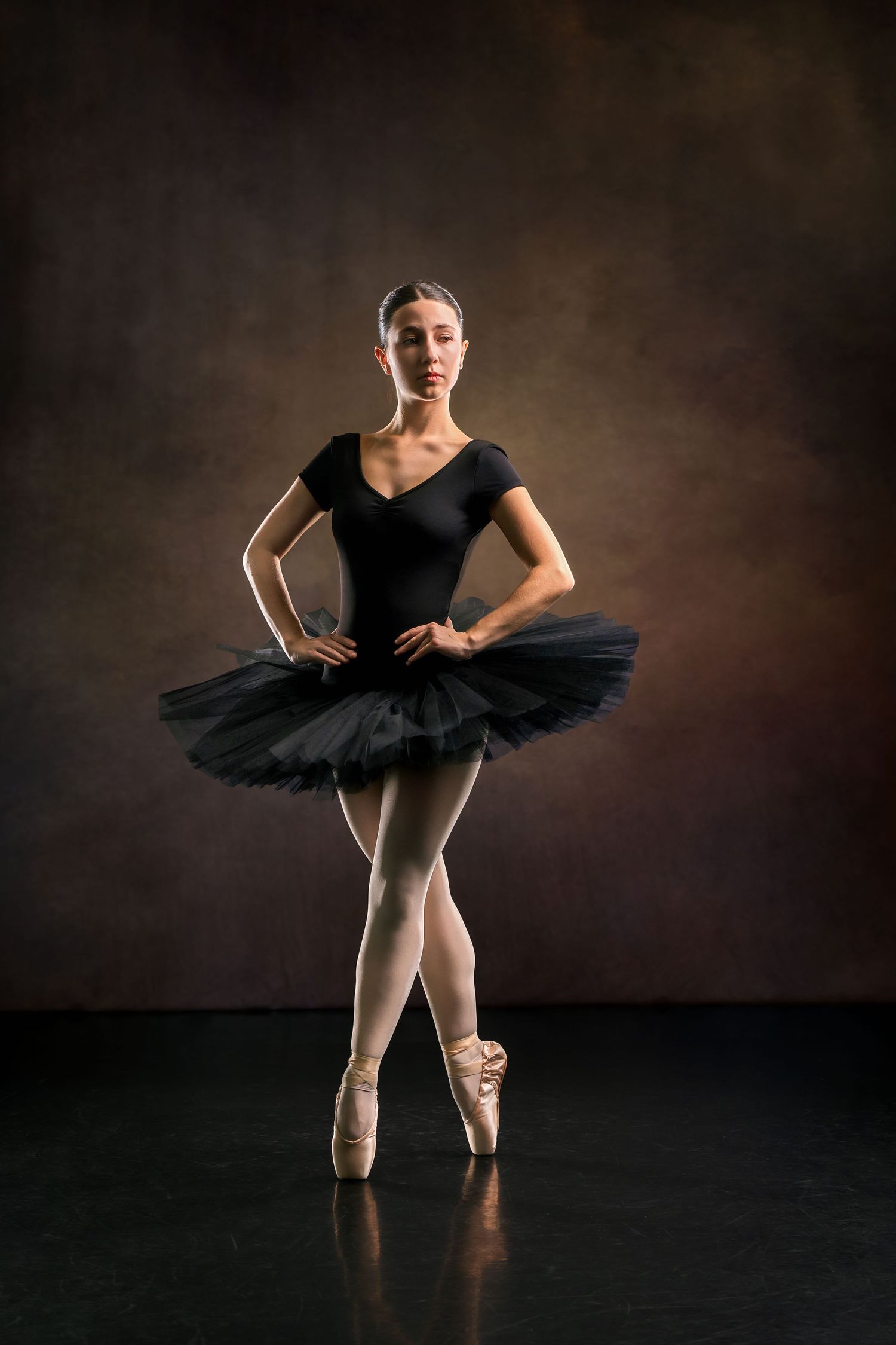Ballerina in black tutu stands en pointe in dramatic studio portrait lighting.