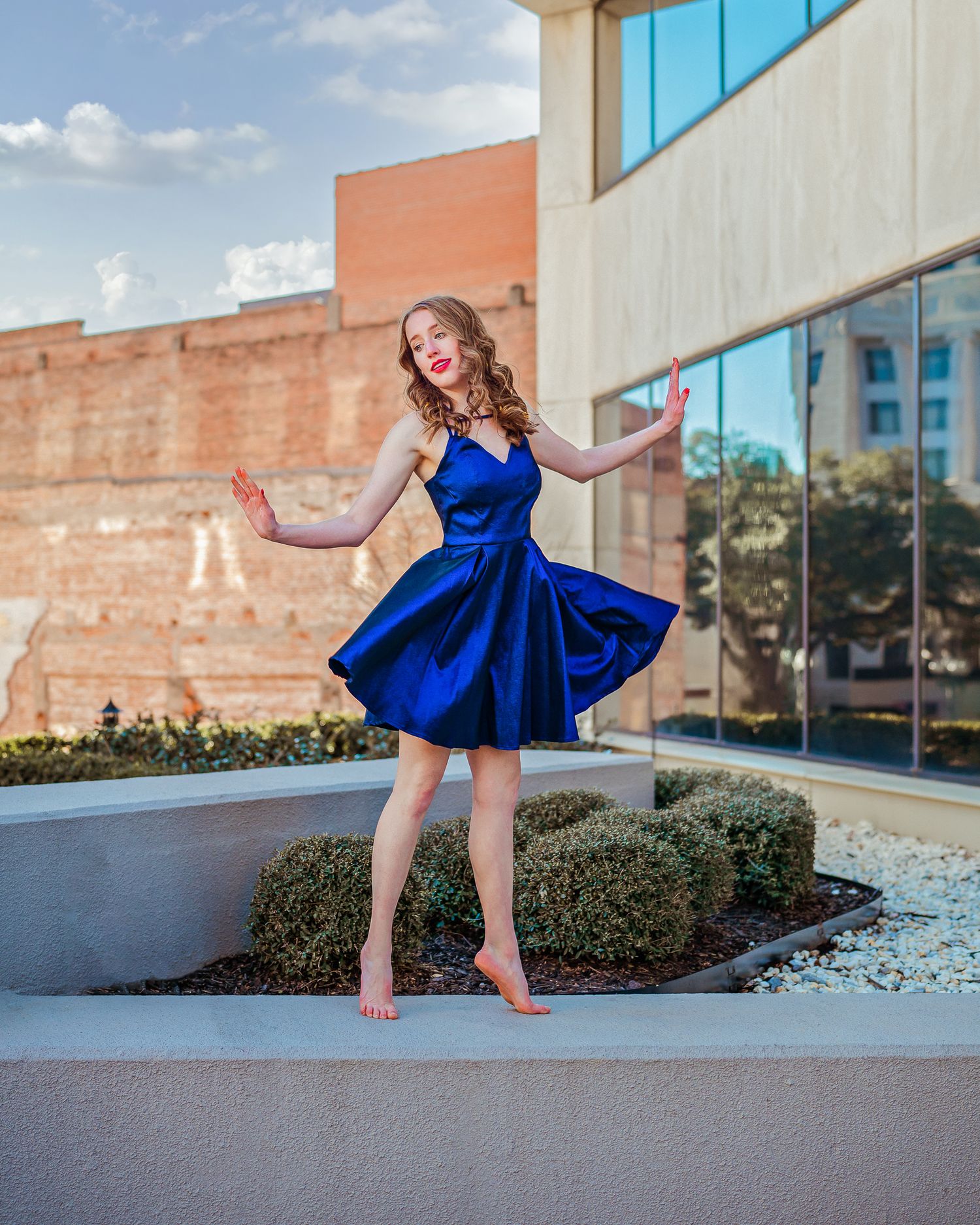 Young woman in blue satin dress dancing outdoors near modern building.