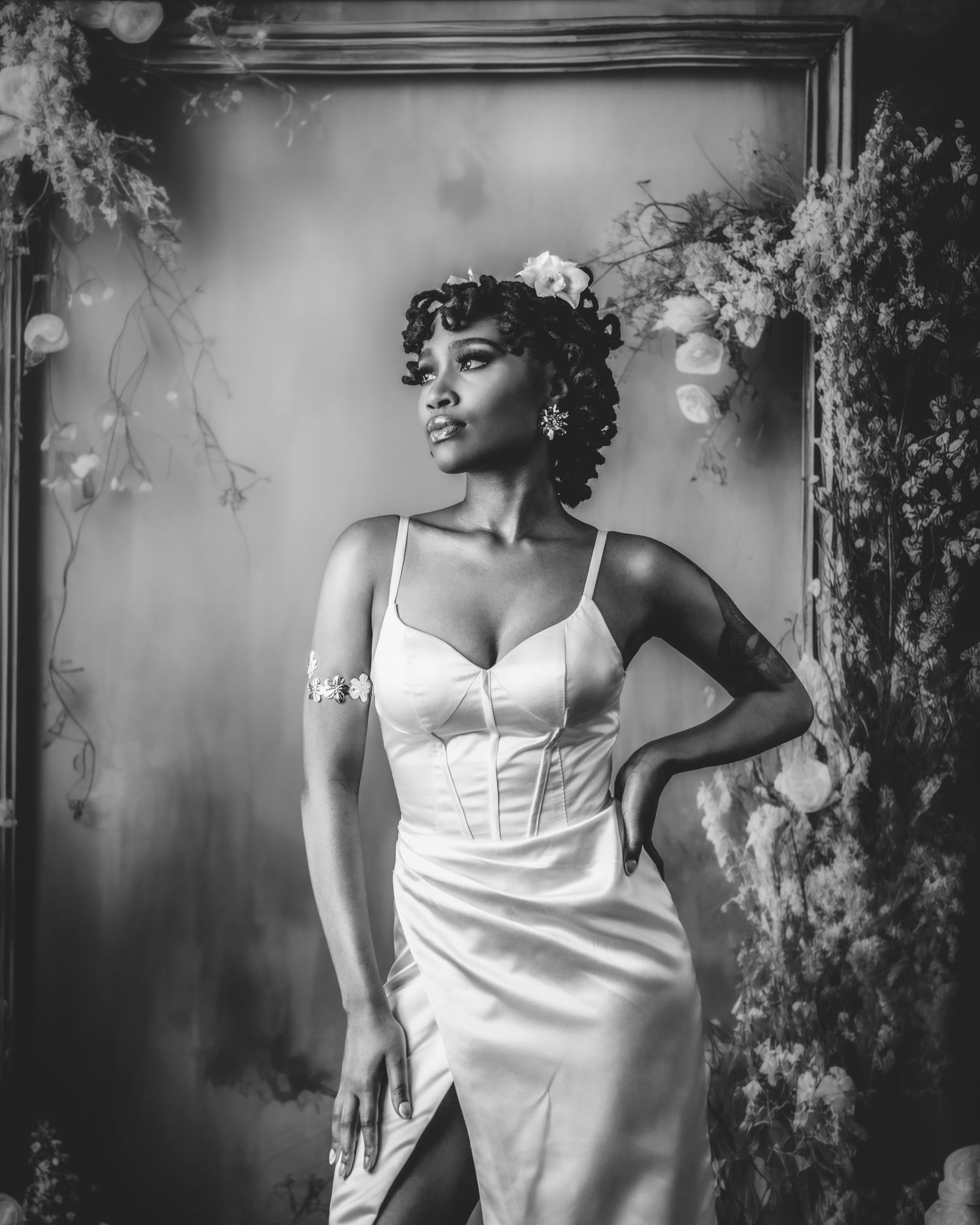 Black and white portrait of woman in white satin dress with floral backdrop.