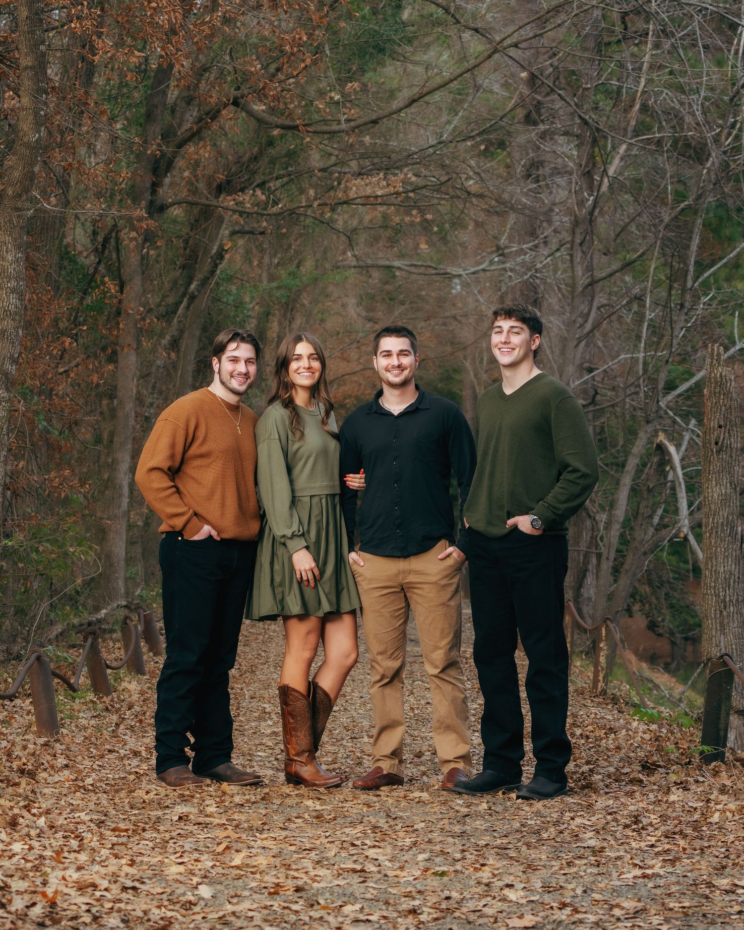 Four young adults posing together on a scenic autumn forest trail in coordinating earth-tone casual outfits.